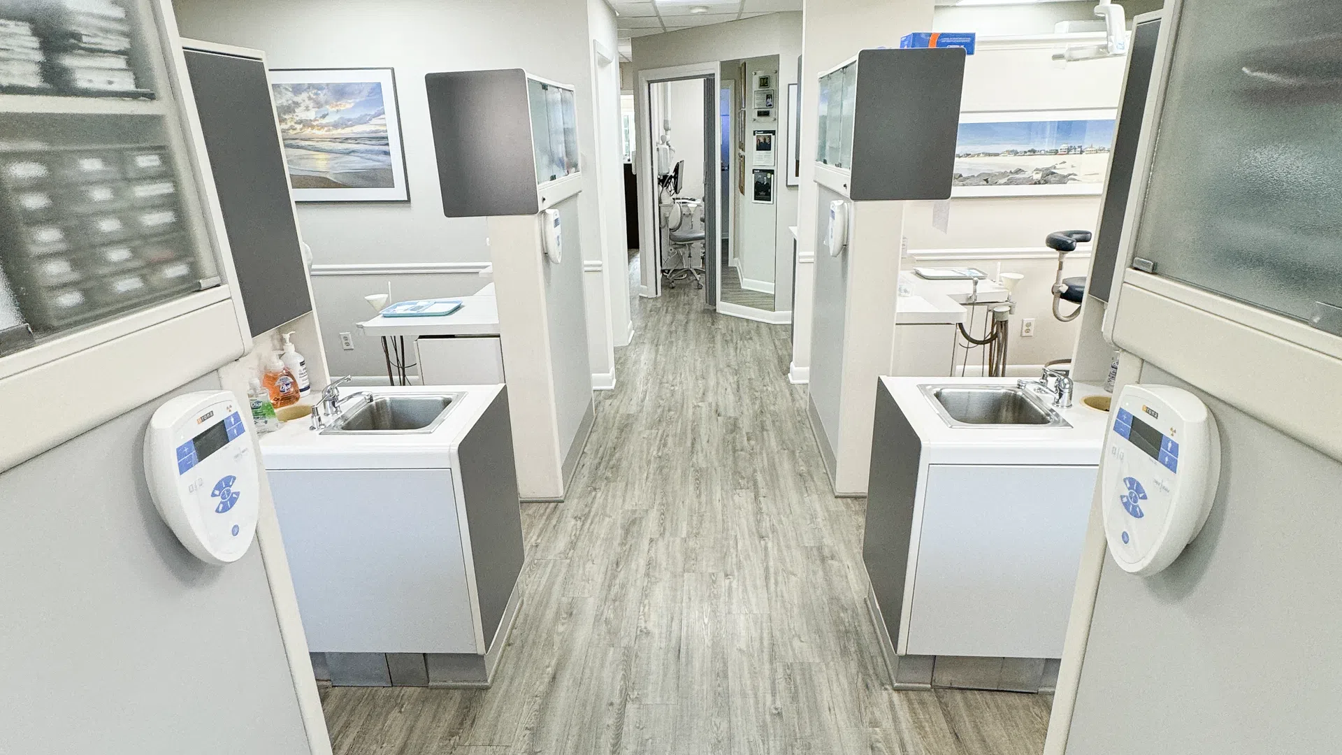 Clean and modern dental clinic hallway with individual treatment stations and wood-effect flooring under bright ceiling lights.