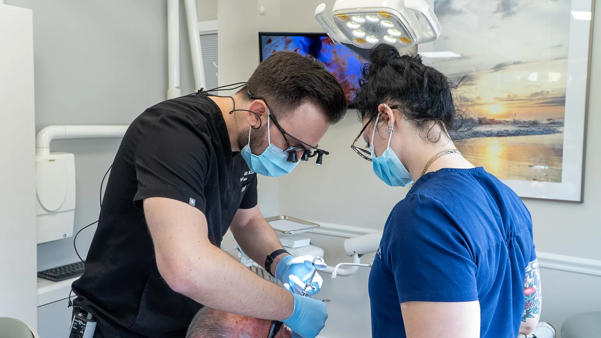Dentist and dental assistant wearing masks performing a dental procedure on a patient in a clinic.