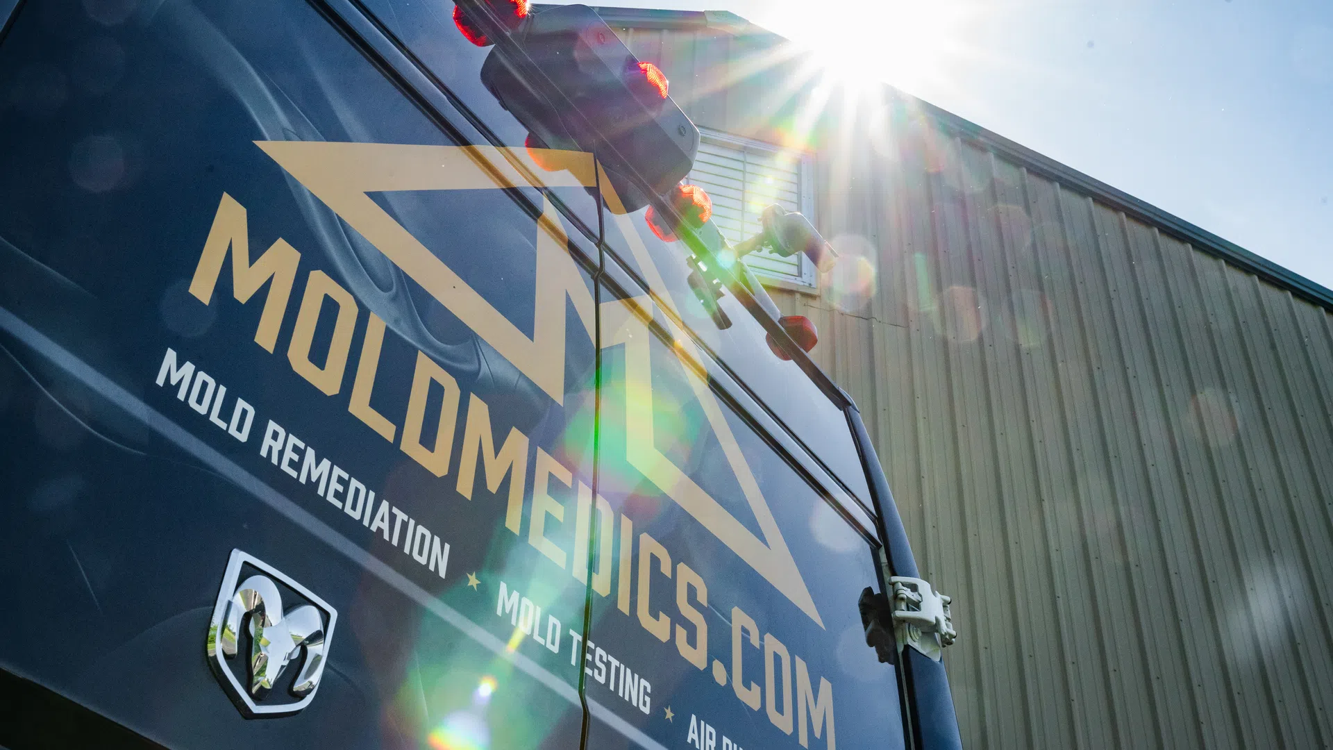 Sunlit black van with MOLMEDICS.COM logo parked outside industrial building under clear blue sky