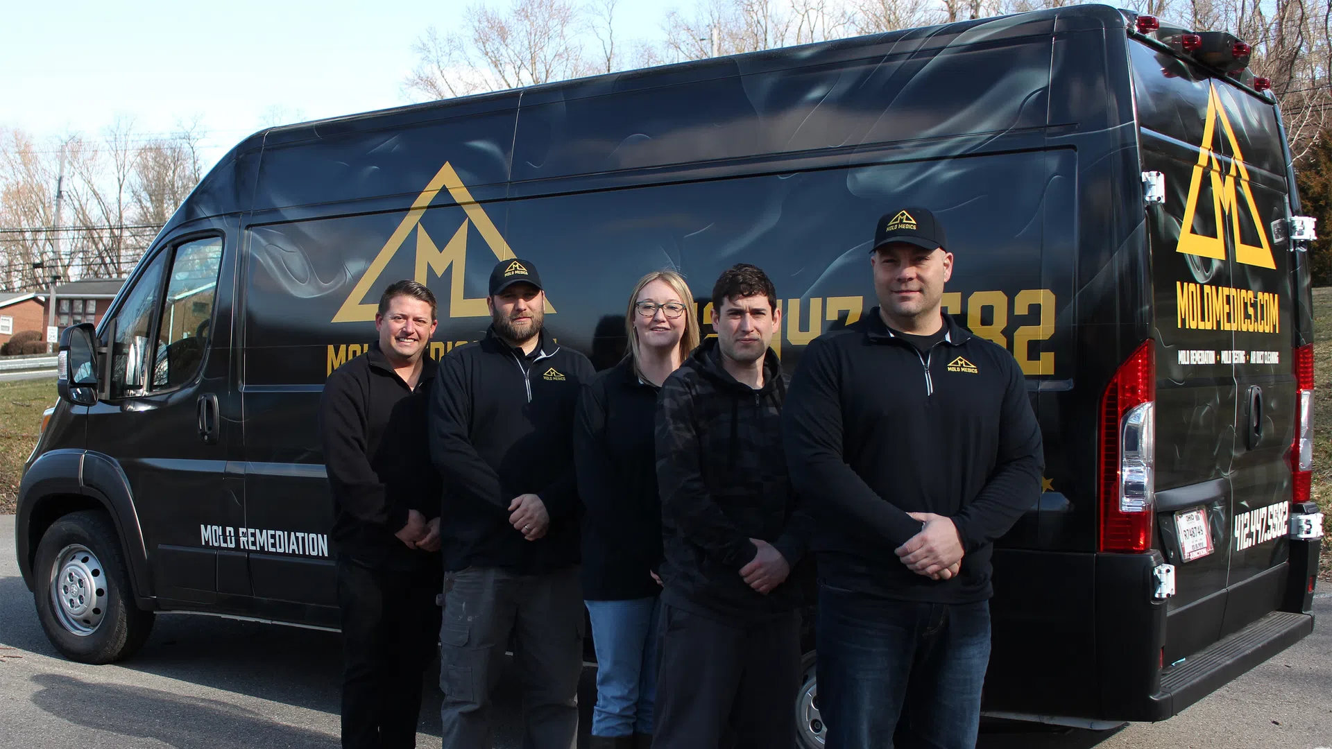 Five Mold Medics team members standing in front of a branded black mold remediation van outdoors.