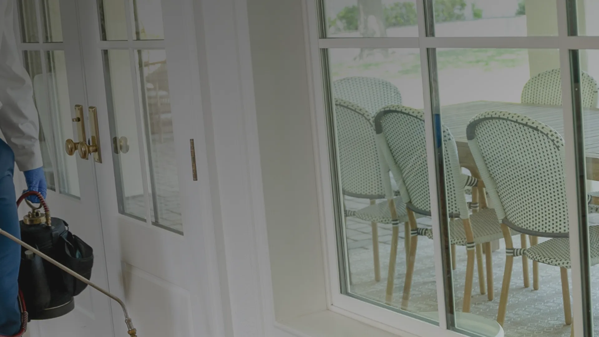 Pest control professional spraying insecticide inside a home near sliding glass doors to a patio.