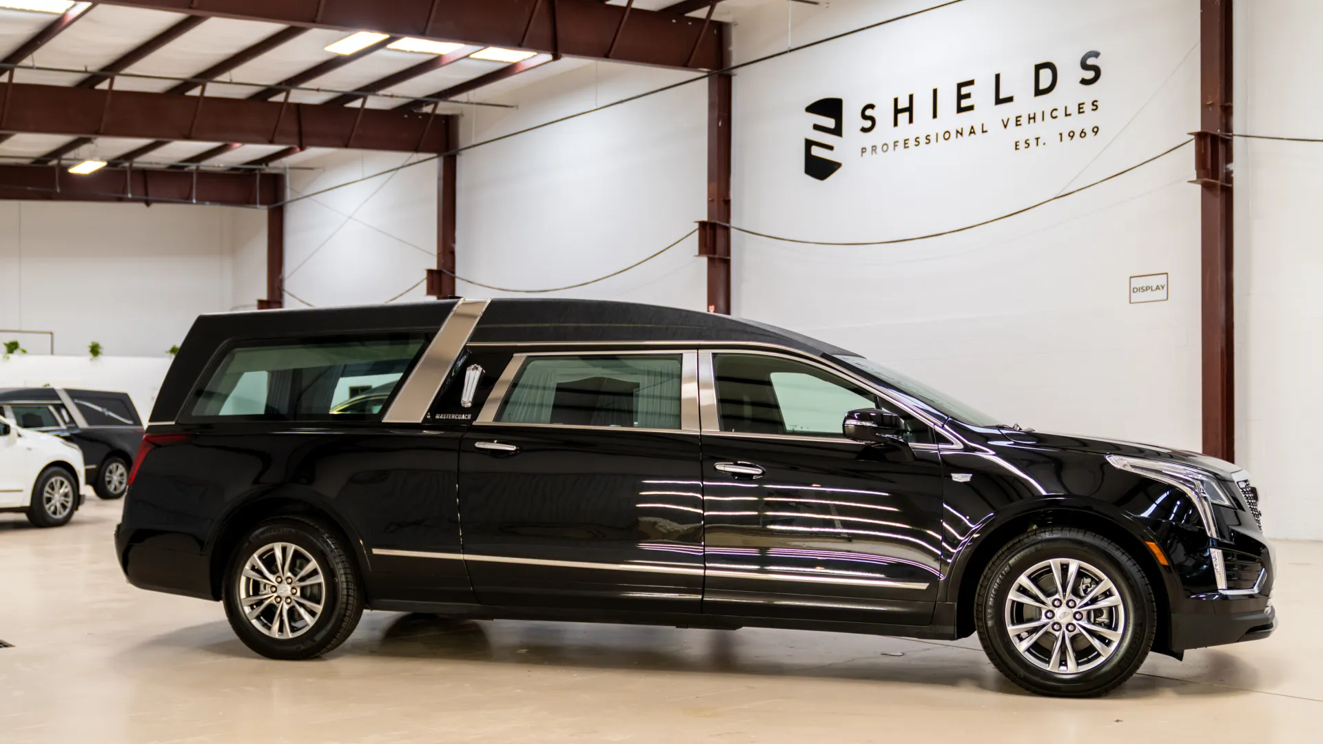 Black luxury professional hearse inside a spacious garage with Shields signage on the wall.