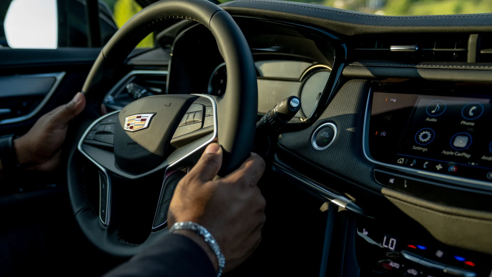 Hands gripping Cadillac car steering wheel with digital dashboard and infotainment screen in focus