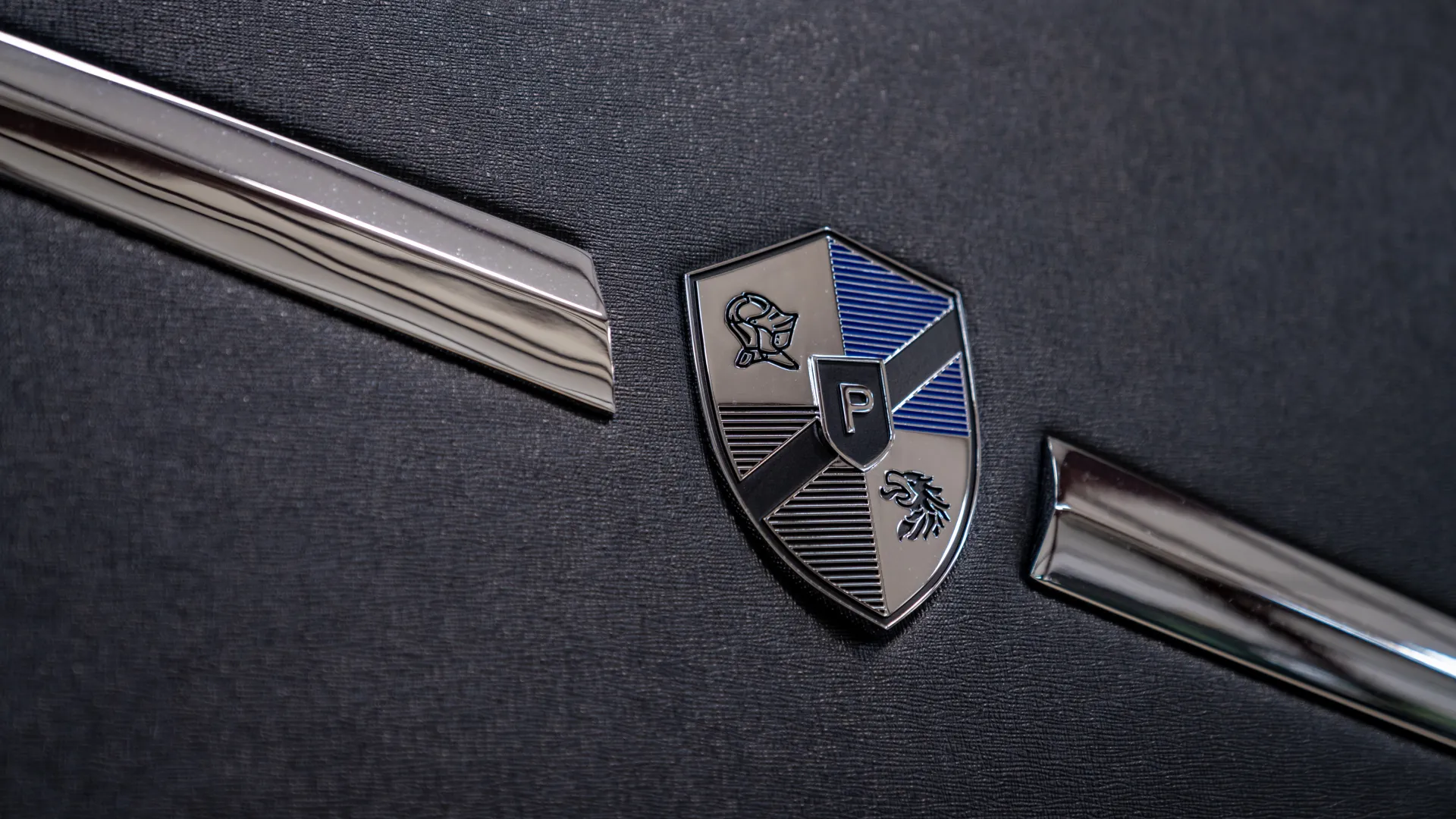 Close-up of a metallic shield emblem with a 'P' and two animal symbols on a textured black surface with chrome accents.