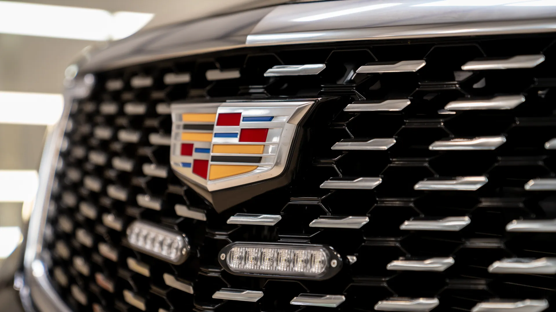 Close-up of Cadillac emblem on a black vehicle grille with silver accents and LED lights.