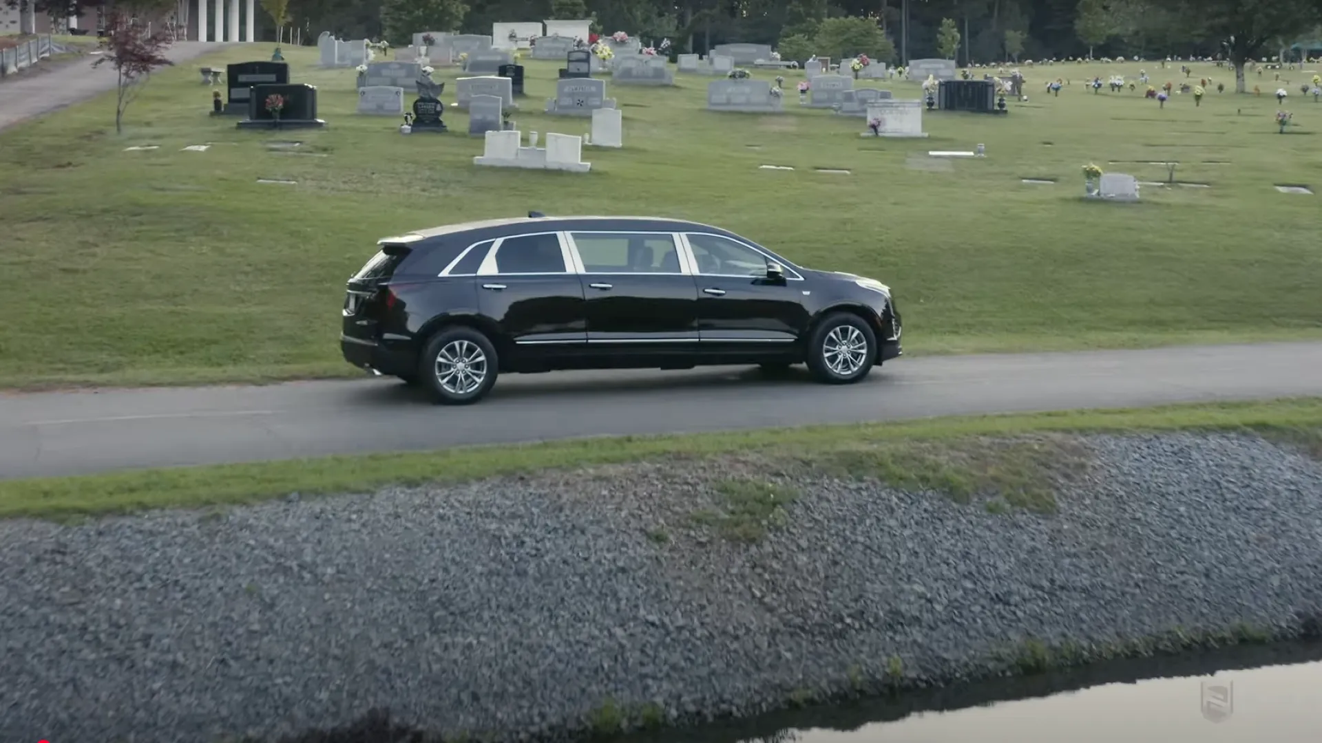 A sleek black SUV driving along a path next to a cemetery, surrounded by gravestones.