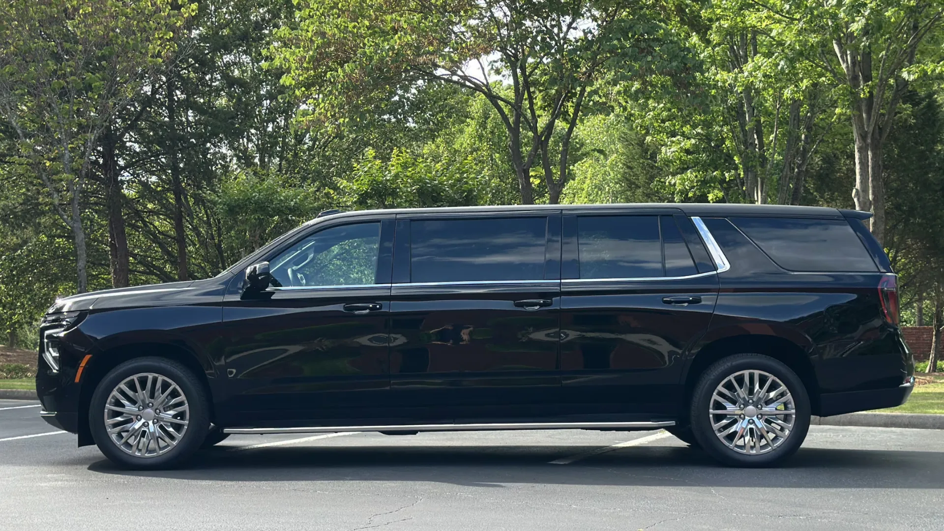 Black luxury extended limousine SUV parked in an outdoor setting with trees in the background