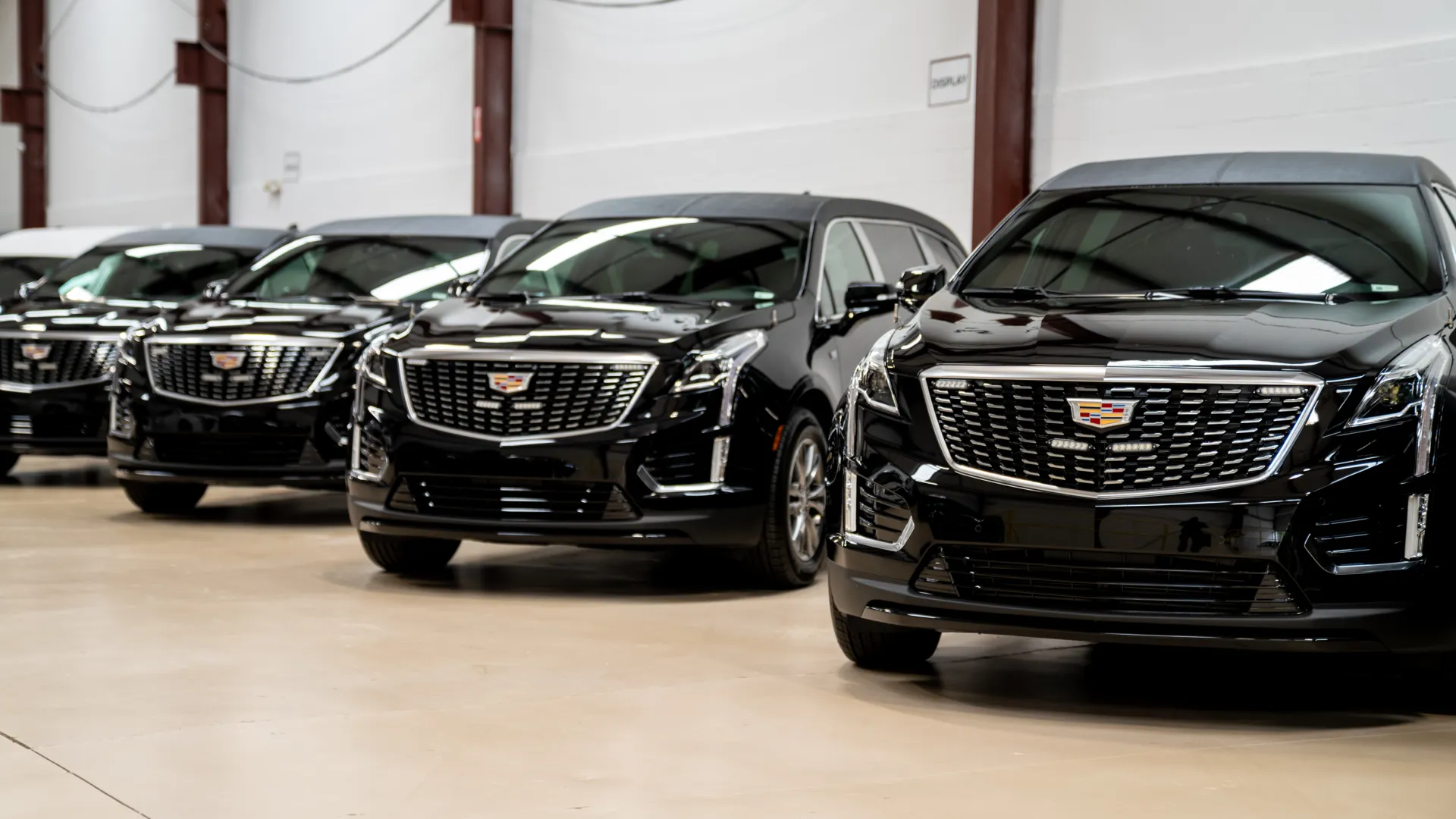 Row of shiny black Cadillac SUVs parked indoors with prominent front grilles and logos in a well-lit showroom.