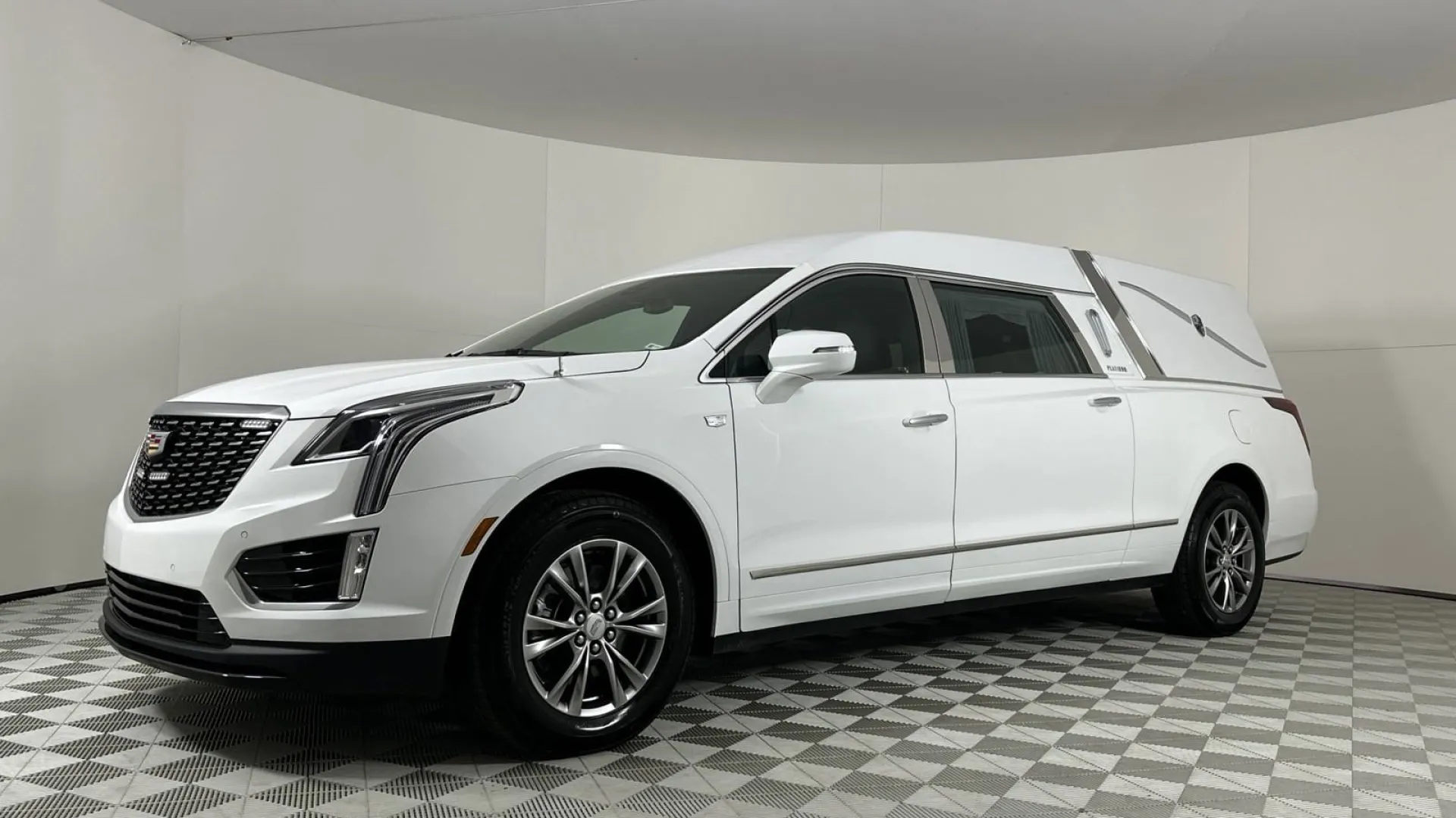 A sleek white hearse parked in a spacious, well-lit showroom with a checkered floor.