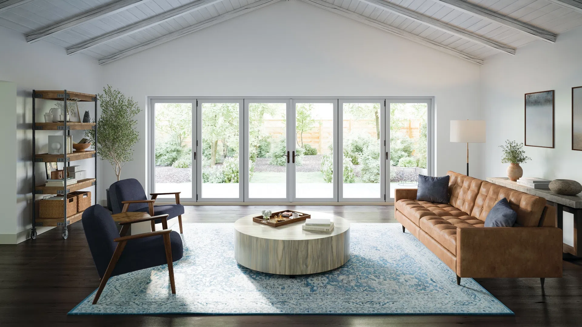 Bright modern living room with leather sofa, navy armchairs, round coffee table, and large glass doors overlooking garden