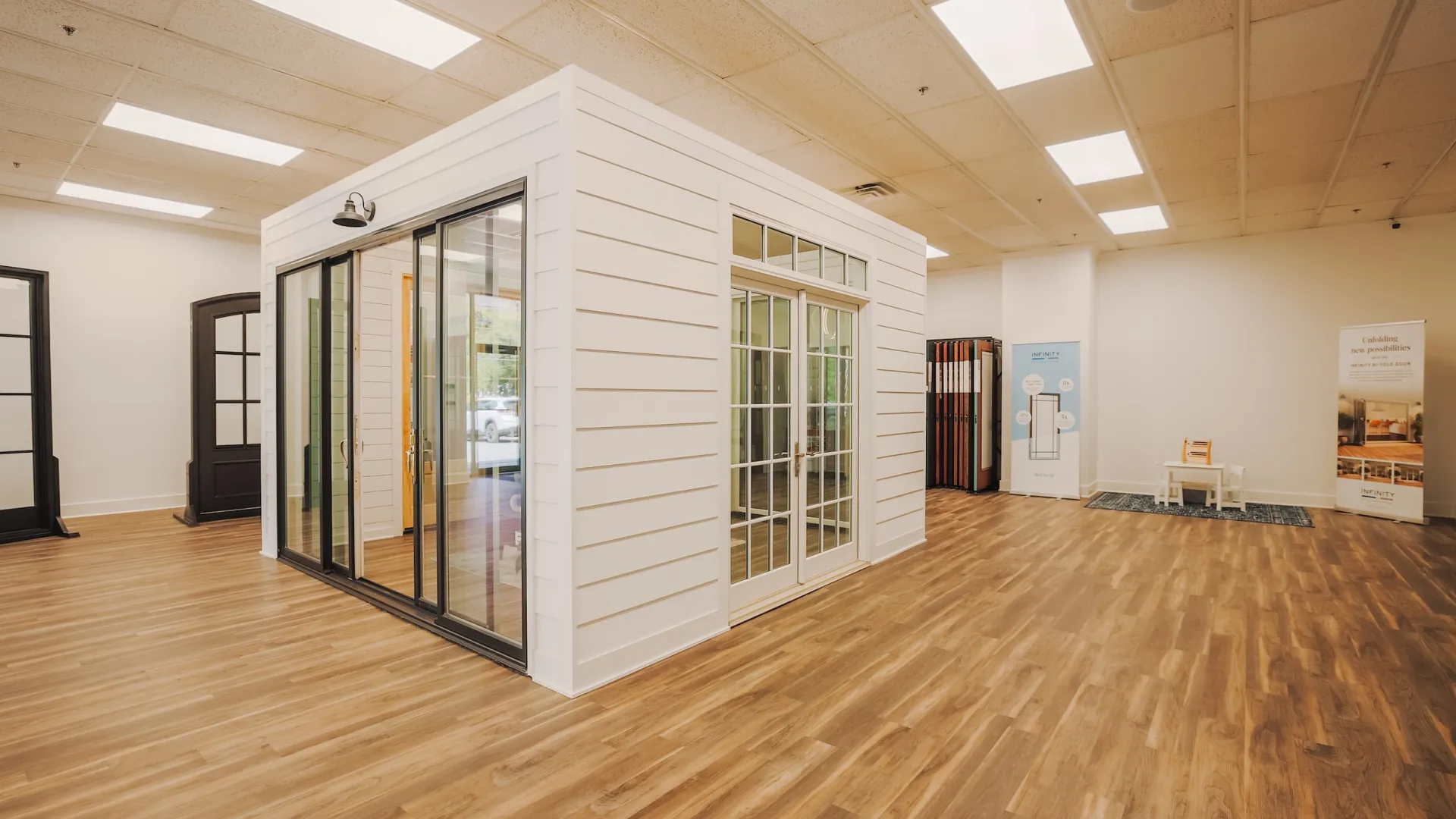 Spacious indoor showroom with wood flooring and white display structure featuring glass doors and windows.