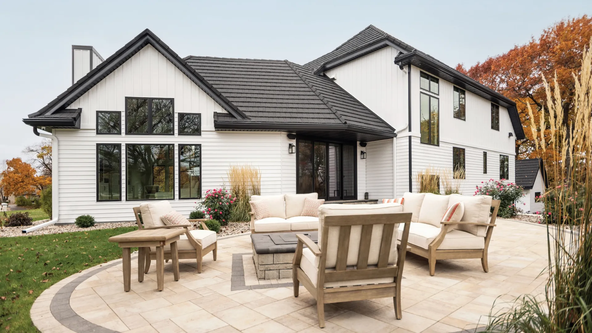 Modern white two-story house with black roof and spacious patio featuring outdoor furniture and fire pit.