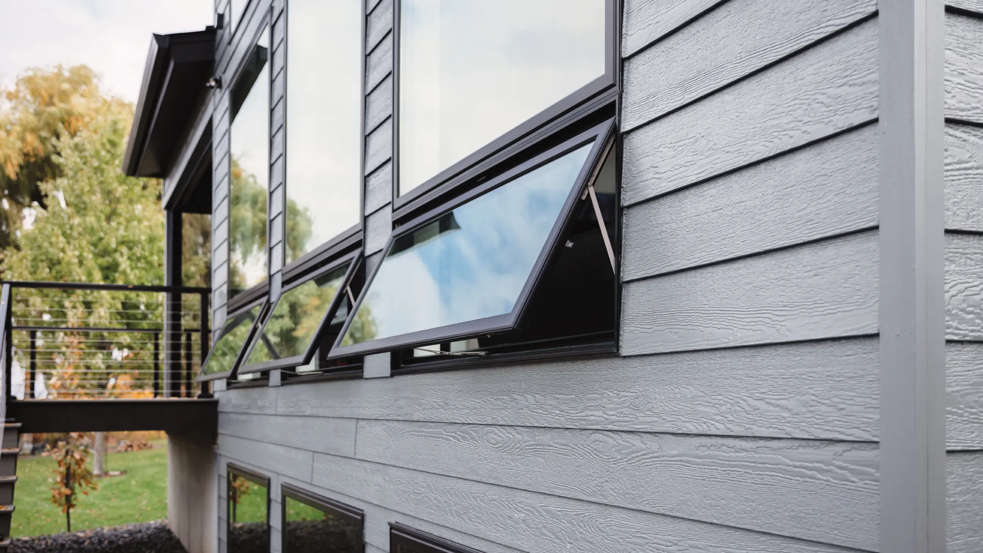 Modern house exterior with large windows and open awning window design on a sunny day.