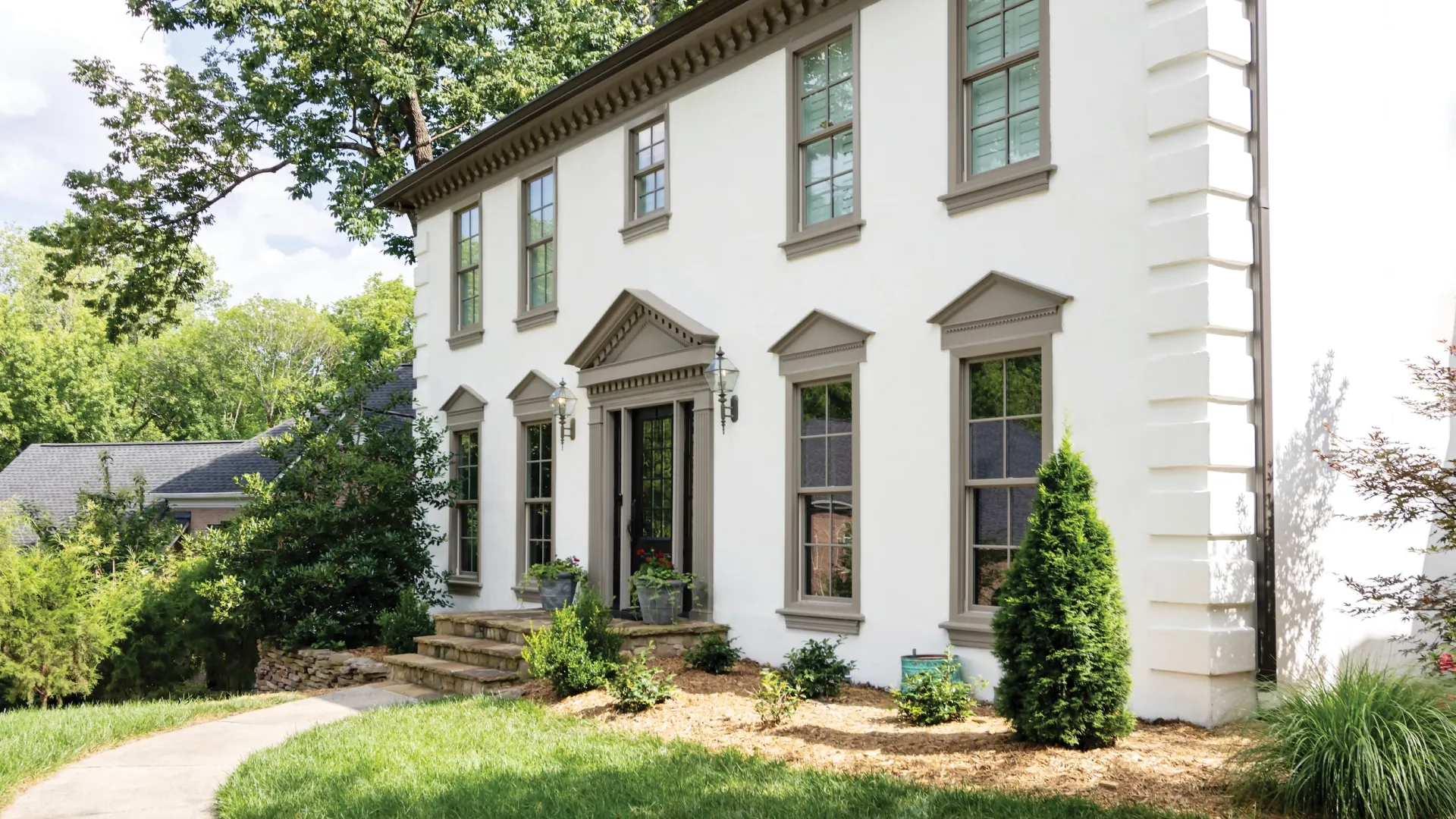 White two-story colonial house with tall windows, a black front door, and a landscaped front yard with shrubs.