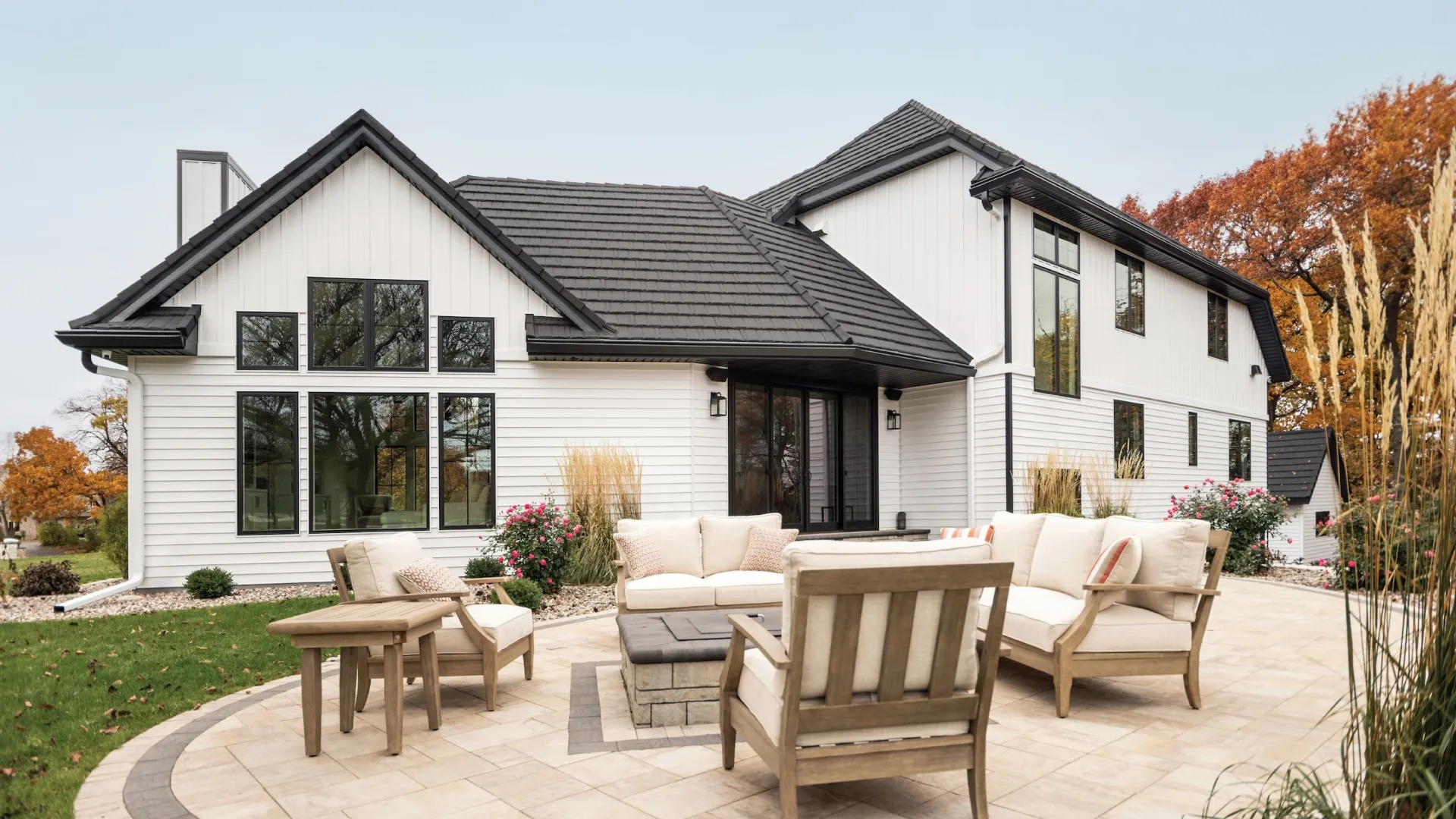 Modern white two-story house with black roof and spacious outdoor patio seating area with cushions and table.