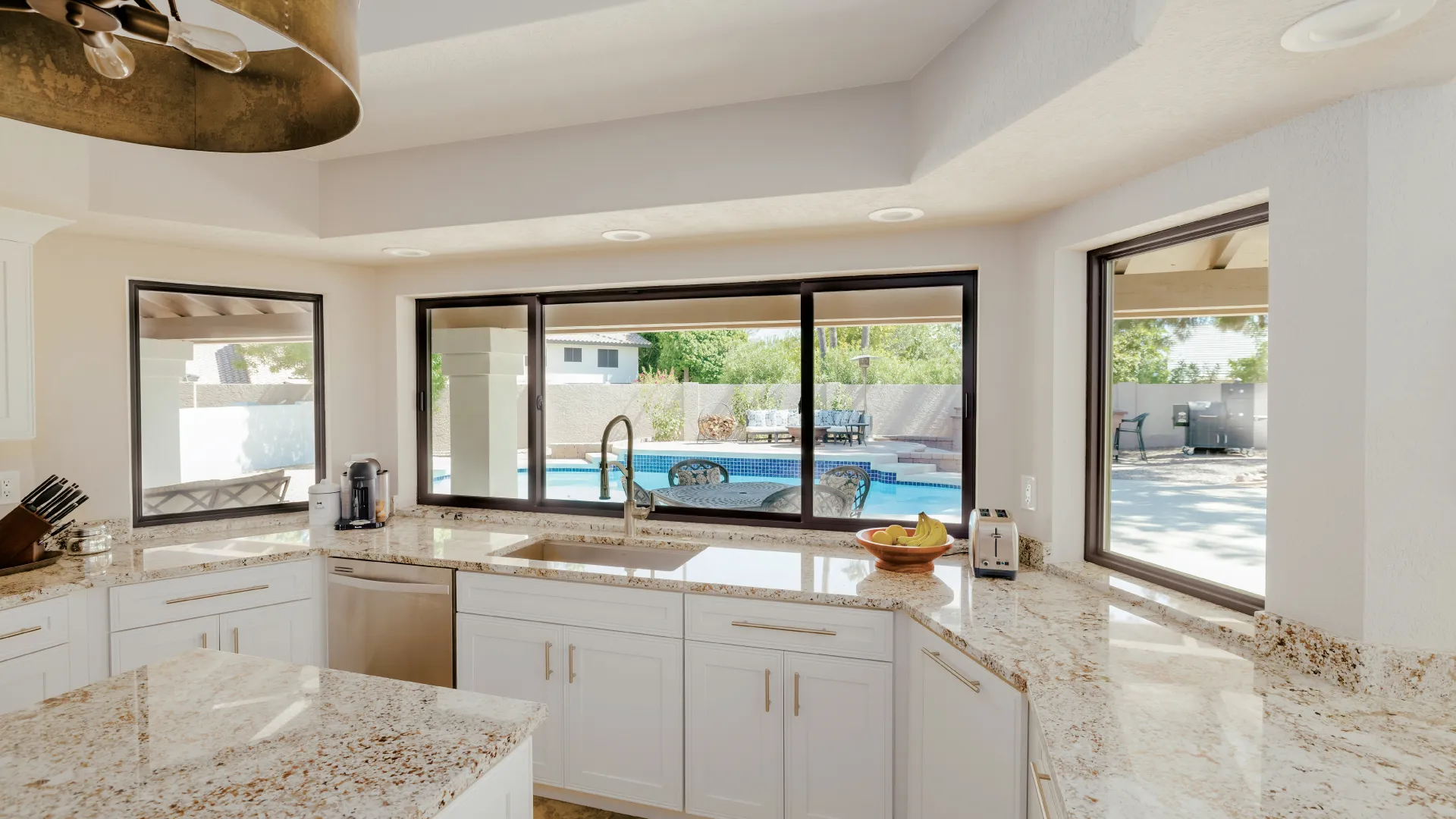 a kitchen with white cabinets and bronze slider windows in front of kitchen sink