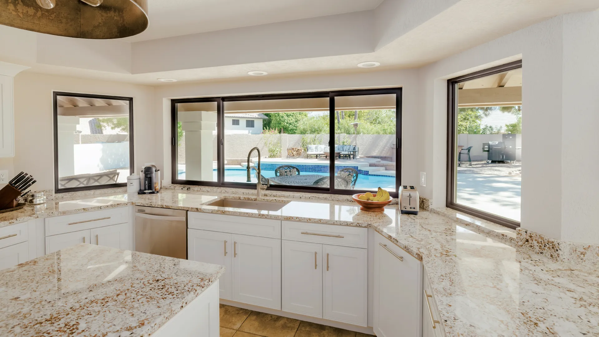 a kitchen with white cabinets and bronze slider windows in front of kitchen sink