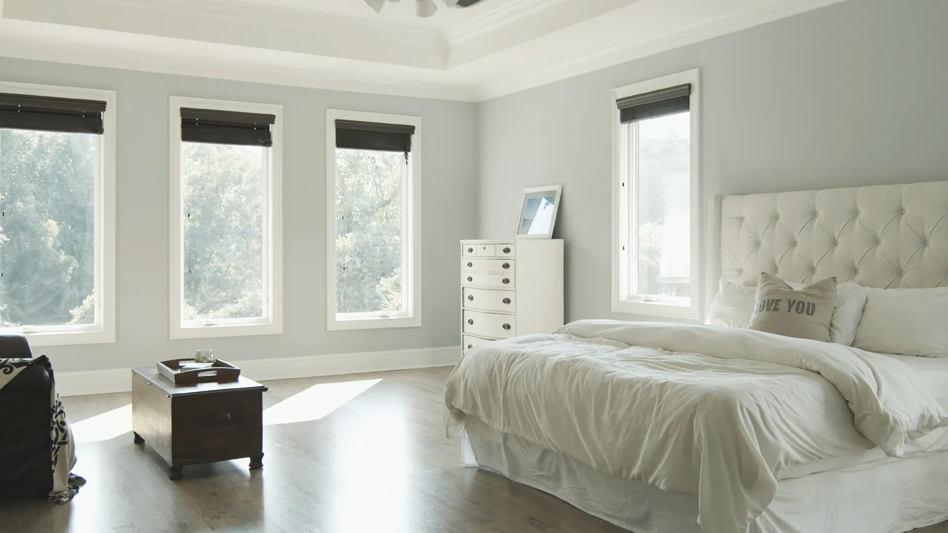 Bright and airy bedroom with white bedding, large windows, and a classic dresser for a serene ambiance.