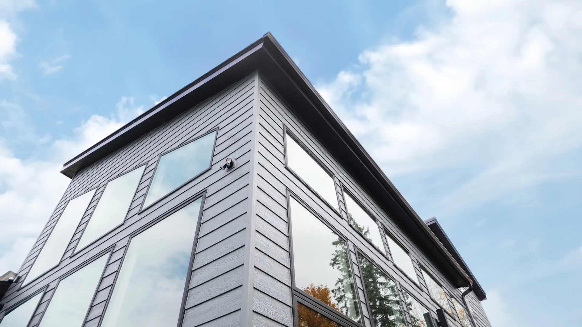 Modern building corner with large reflective glass windows under a partly cloudy blue sky.