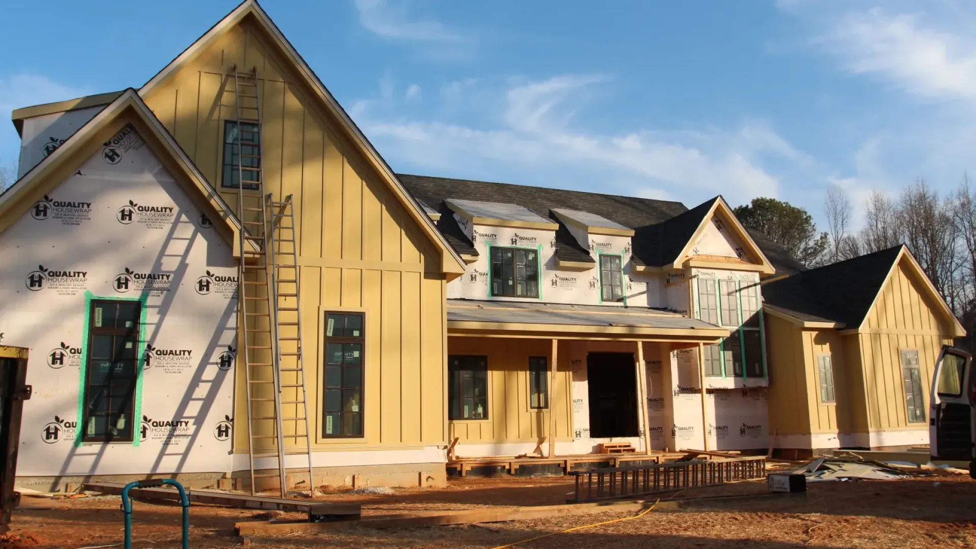 New house under construction with yellow siding and exposed sheathing against a blue sky