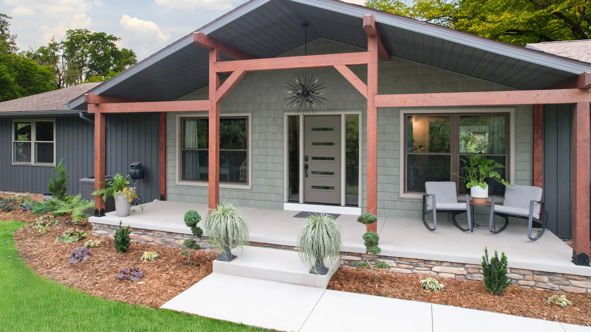 Modern house exterior with gray siding, wooden beams, a covered porch, and landscaped front yard