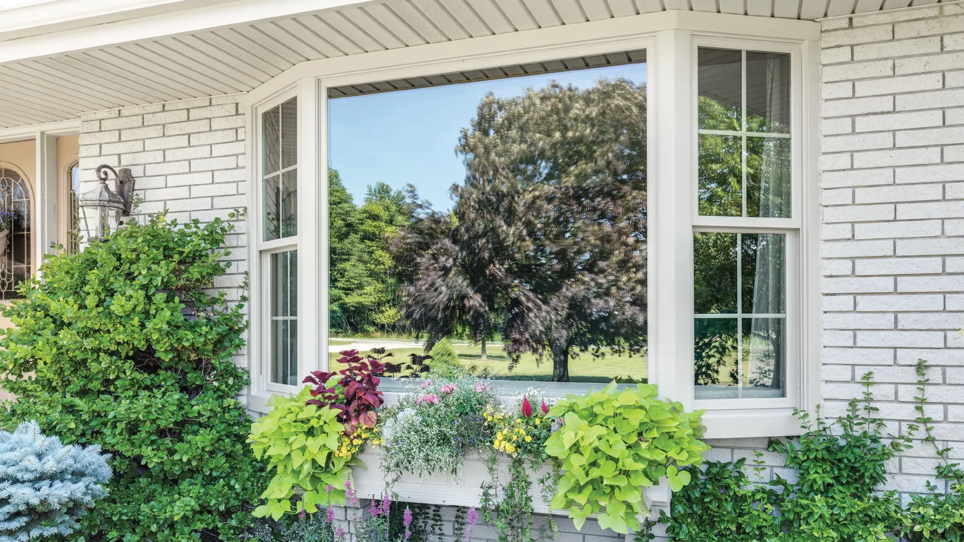 White brick house with white Infinity from Marvin fiberglass bay window with plants in windowwindowboxbox and growing in planter below the bay window.