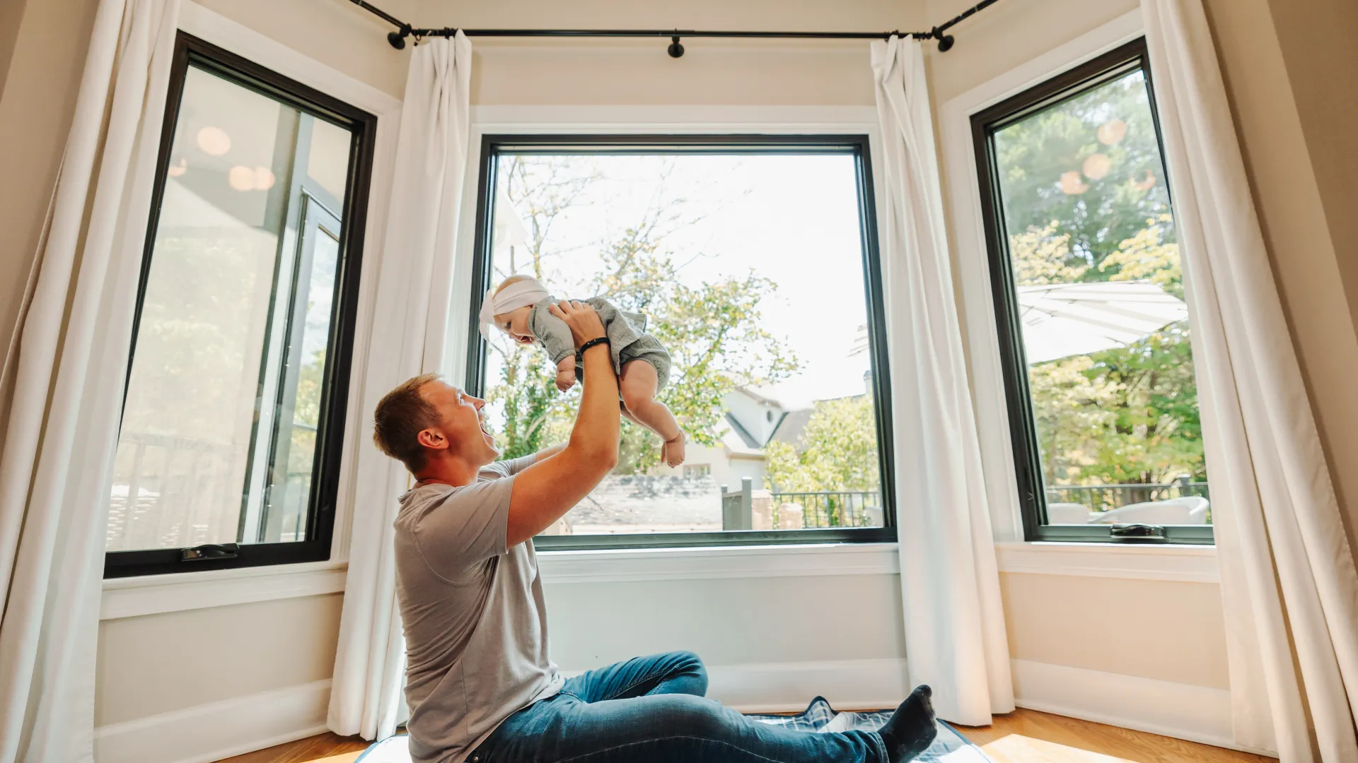 Man plays with baby in front of black fiberglass fixed picture windows