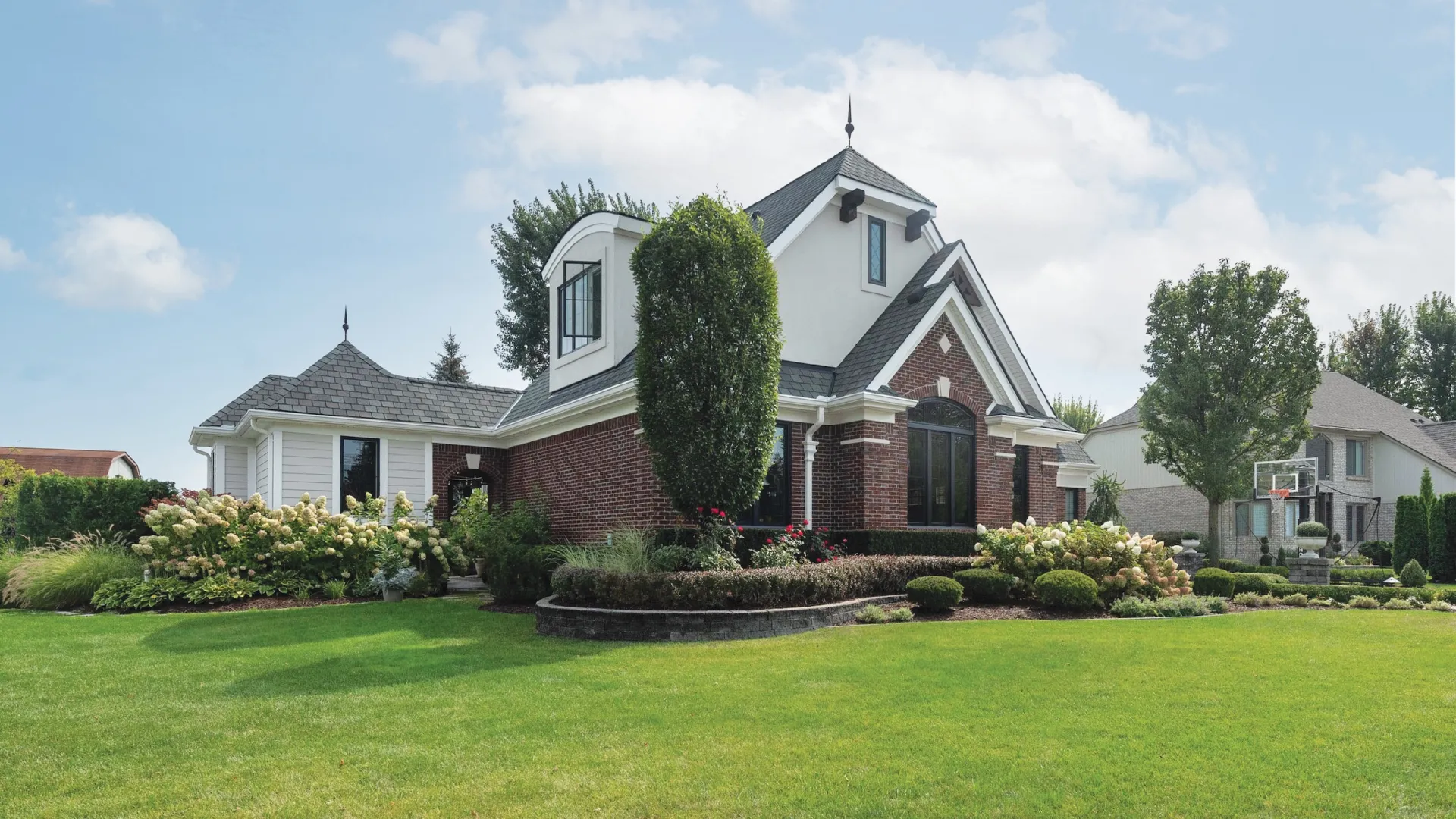 Brick and white modern house with manicured garden and lush green lawn under a partly cloudy sky
