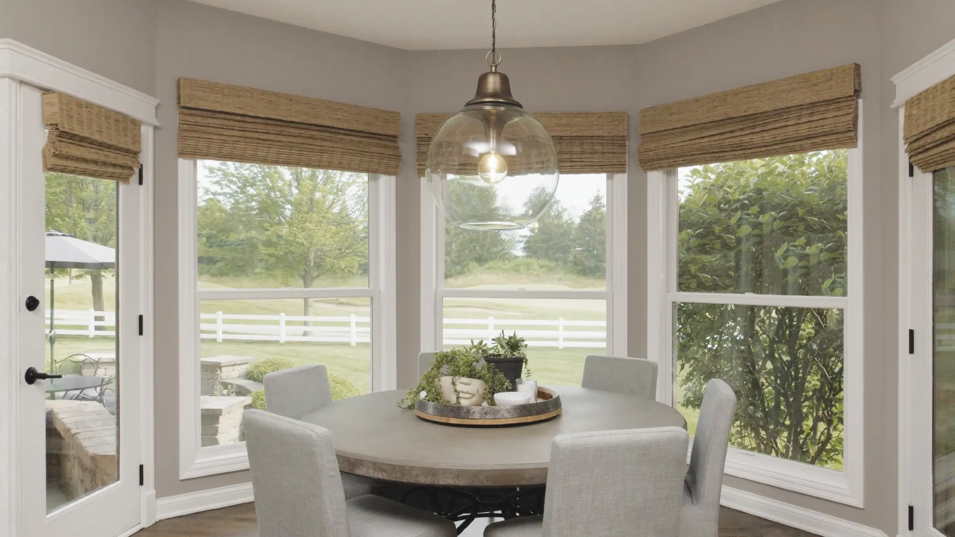 A dining room with a round dining table and three white double hung fiberglass windows overlooking the backyard
