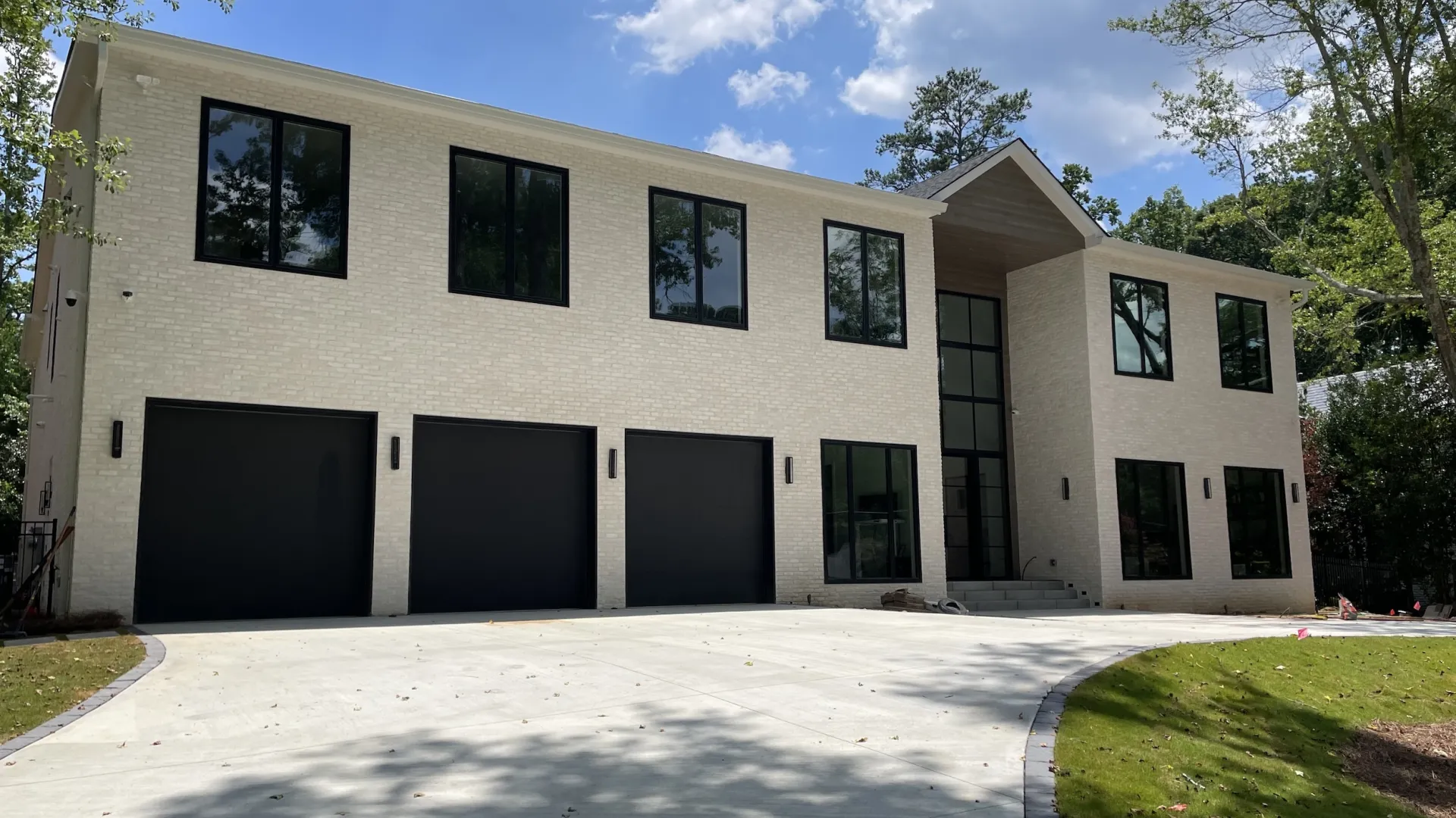 Modern two-story house with large windows, three garage doors, and green lawn under a blue sky.