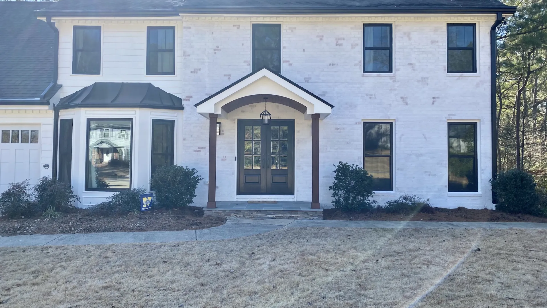 Two-story white brick house with black-framed windows, a bay window, and a centered entrance with a small porch.