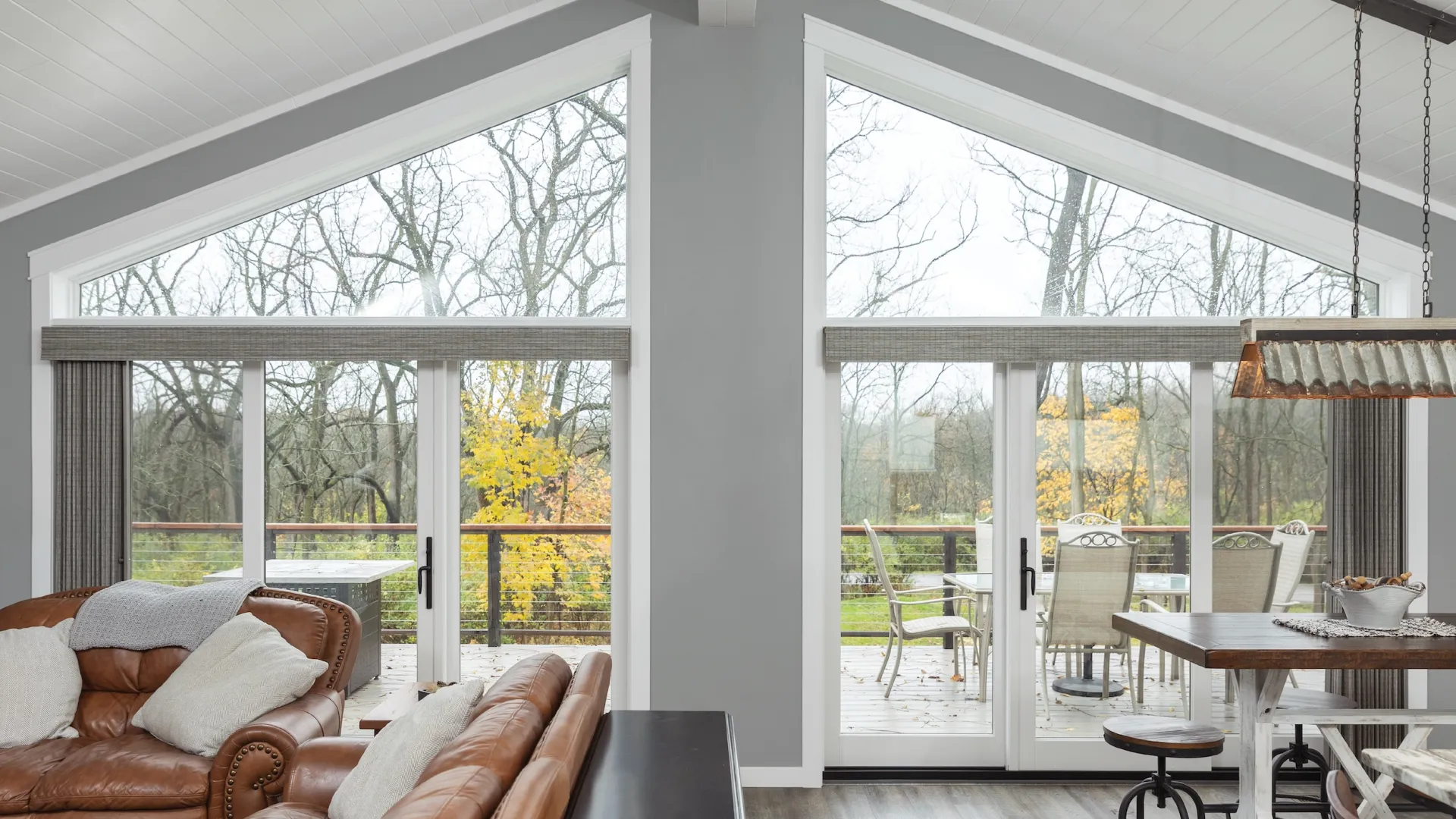 Modern living room with brown leather sofas and large glass doors overlooking a wooded outdoor deck.