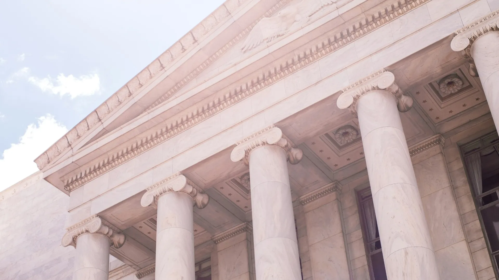 Marble courthouse facade with classical columns and intricate triangular pediment under blue sky