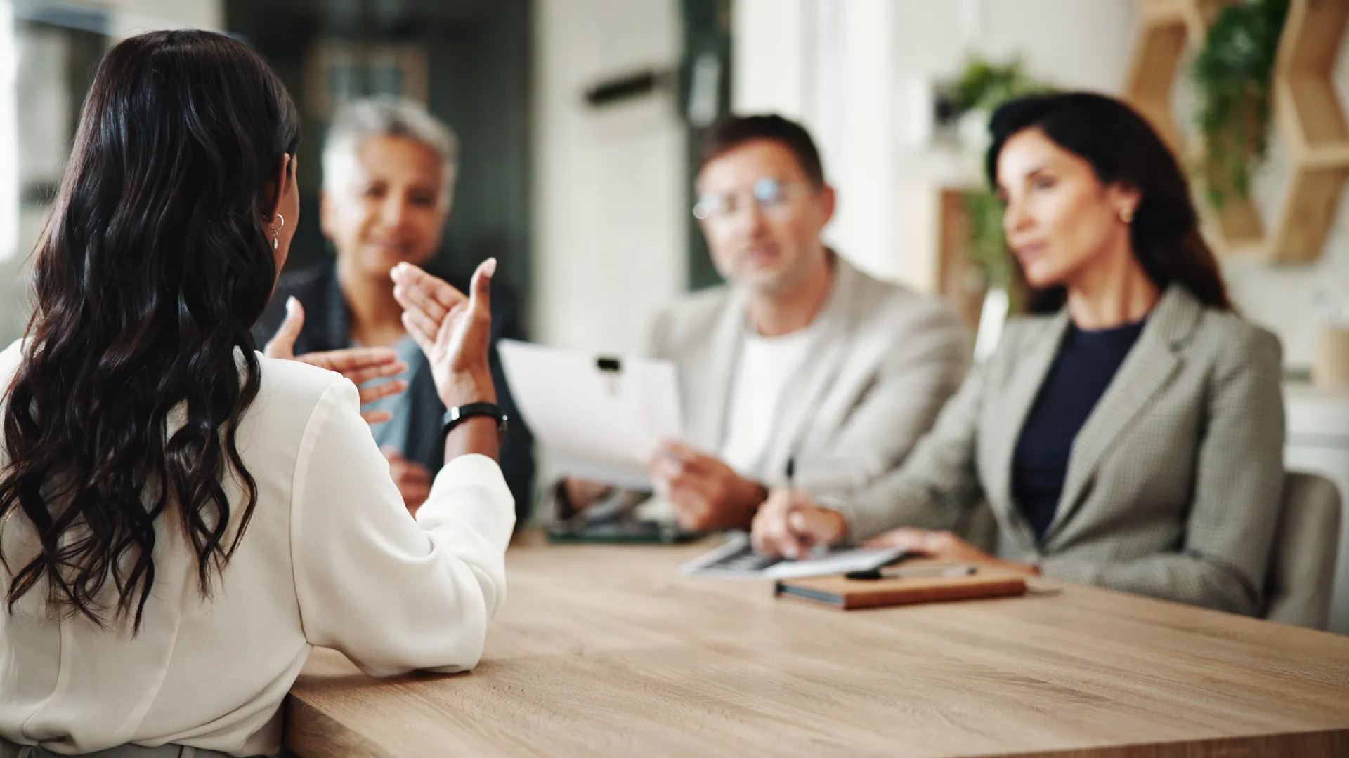 Woman in white blouse explaining to three colleagues during a business meeting around a wooden table.