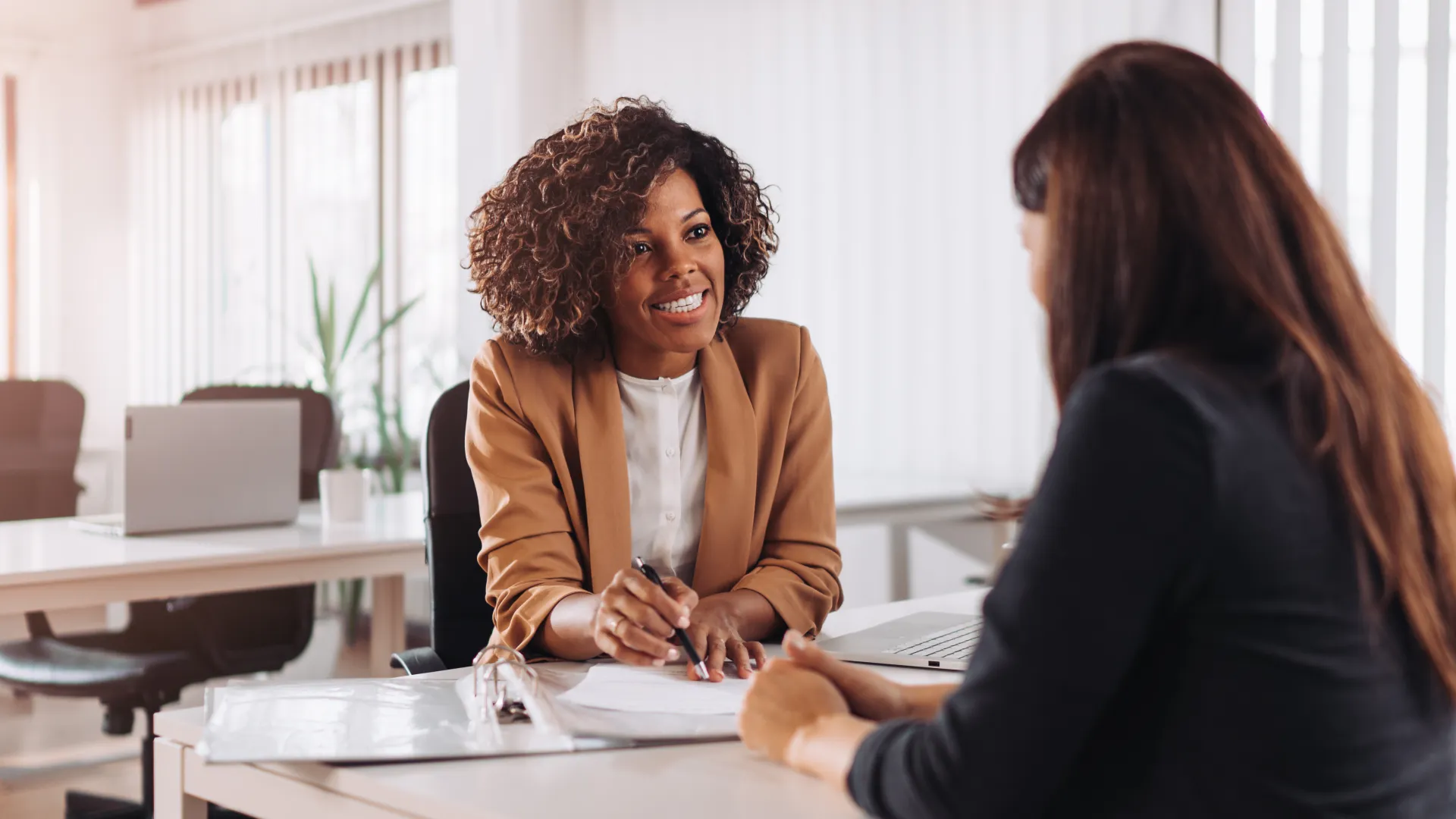 Two professional women having a friendly business meeting in a bright modern office setting.