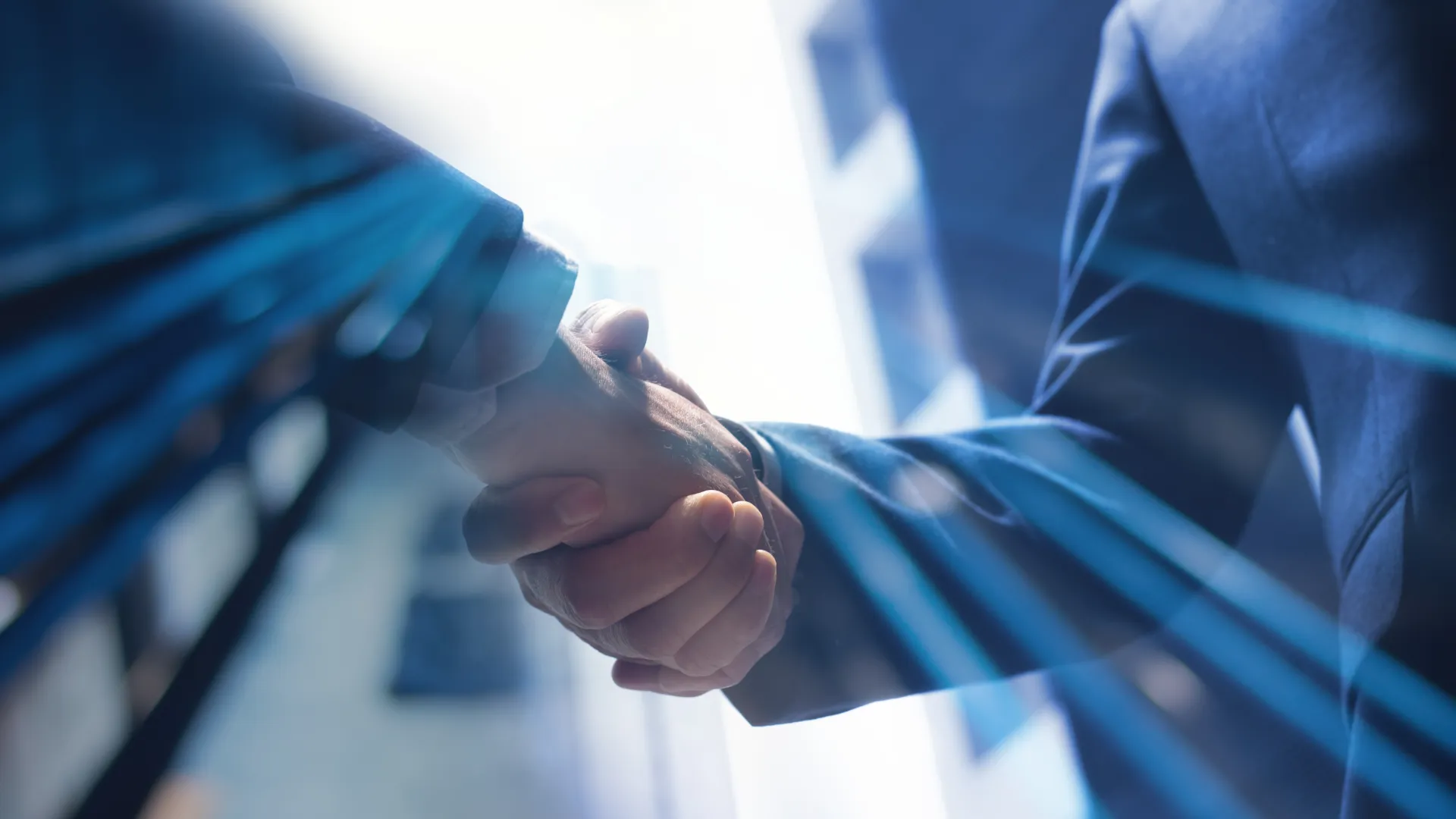 Close-up of two business professionals shaking hands with digital blue lines overlay symbolizing technology and partnership.