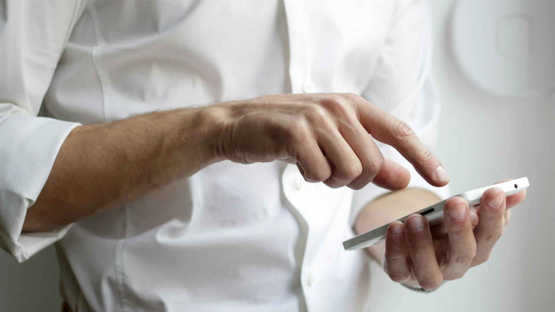 Person in white shirt using a smartphone with one hand tapping the screen indoors.