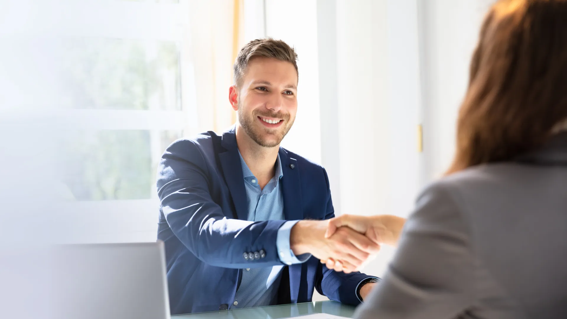 Two professionals shaking hands in a bright office setting, symbolizing business agreement and partnership.