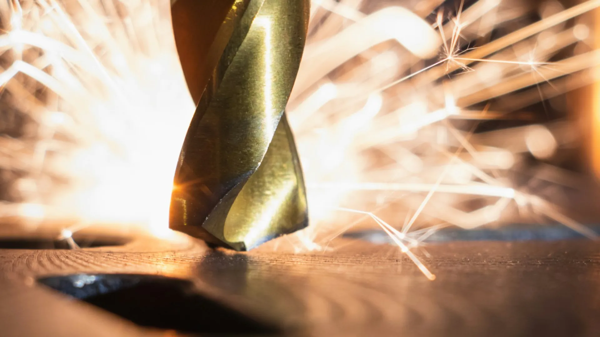 Close-up of a drill bit cutting metal with bright sparks flying around in a workshop setting.