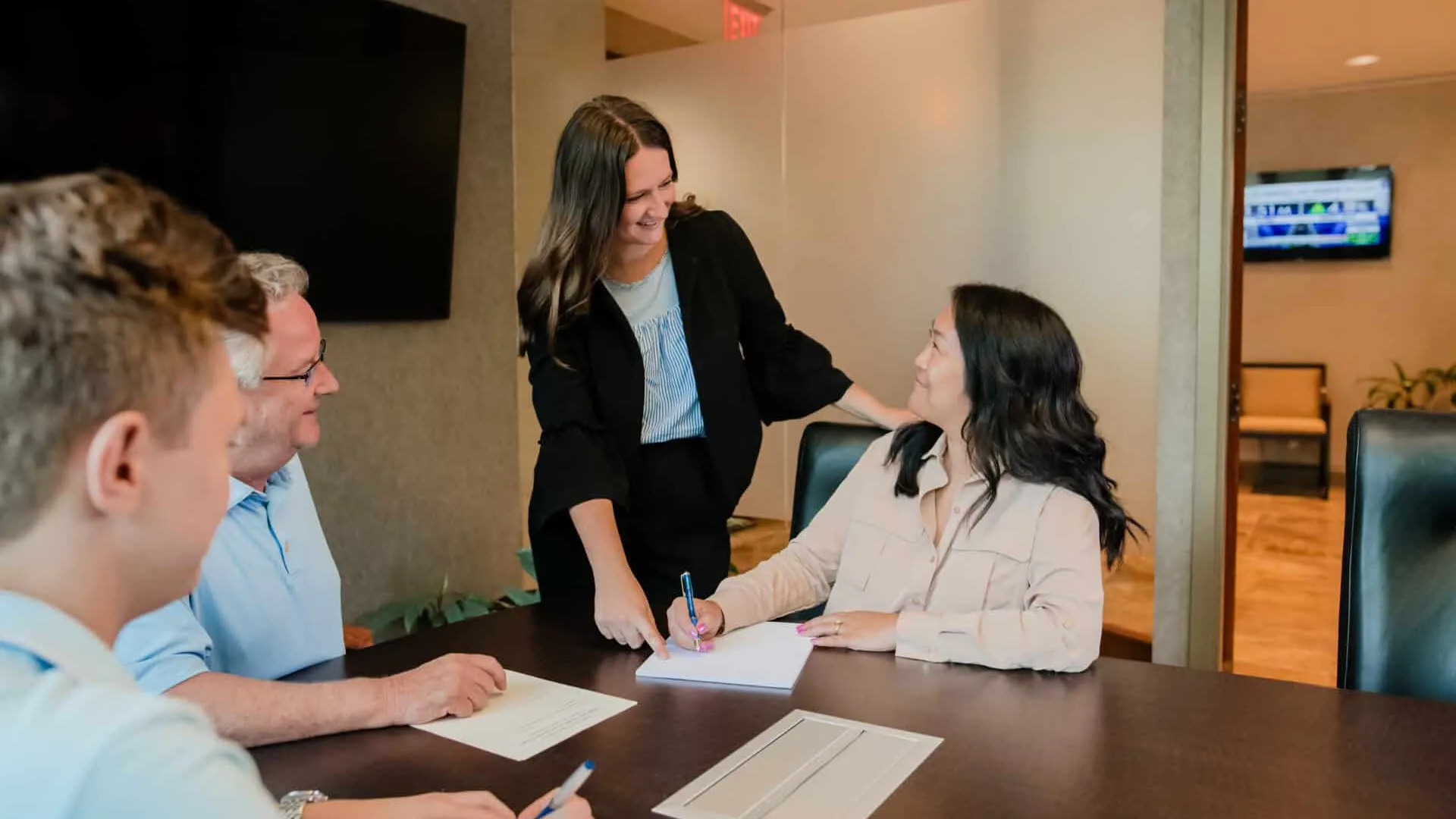 Four professionals engaged in a meeting, smiling and discussing ideas around a conference table with documents and pens.