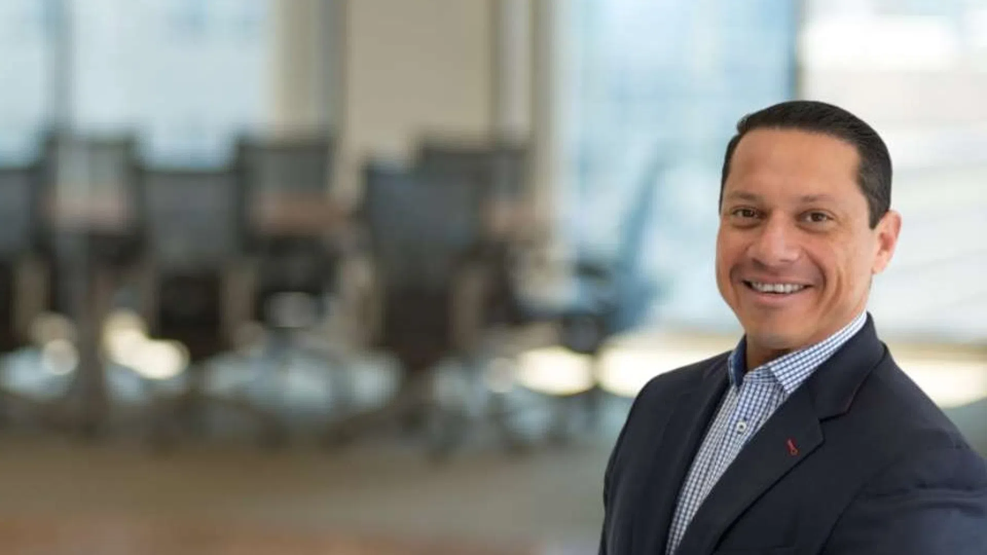 Smiling businessman in a suit standing in a modern office with glass walls and conference room in the background