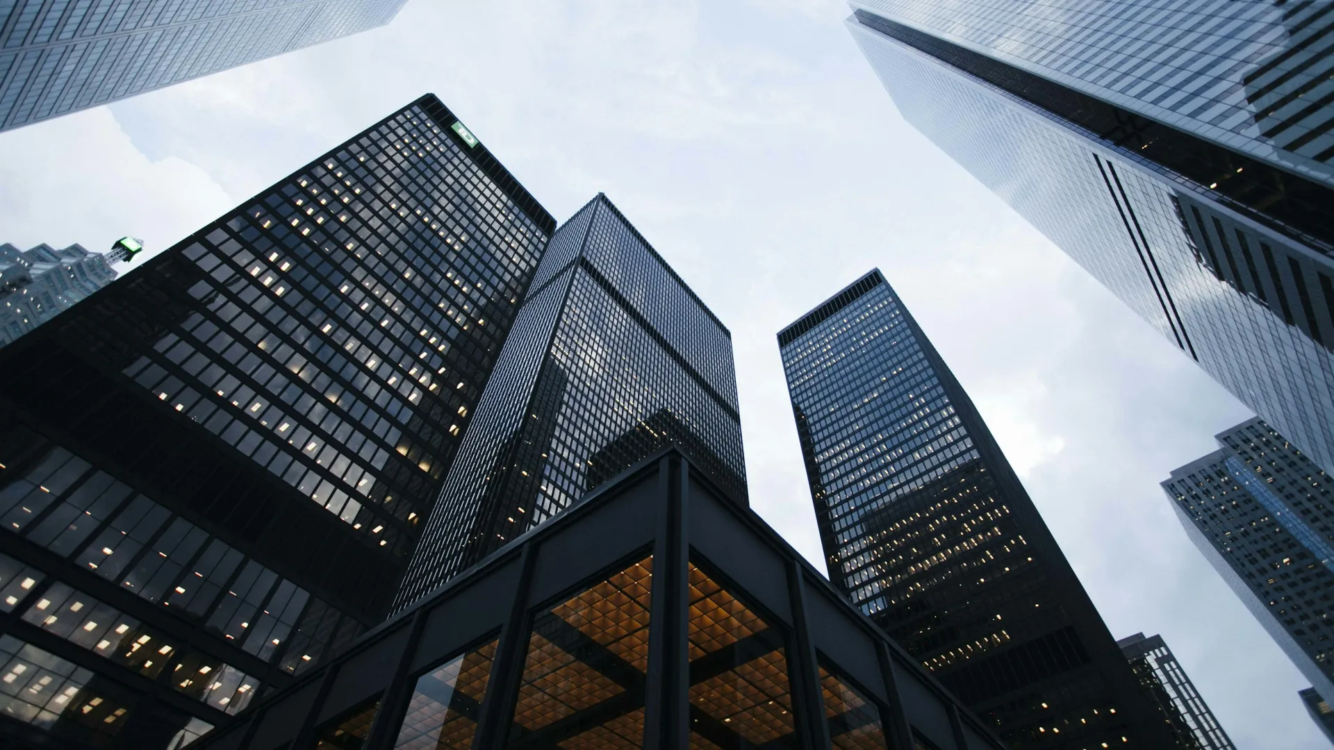 Low-angle view of modern glass skyscrapers against a cloudy sky in an urban cityscape.