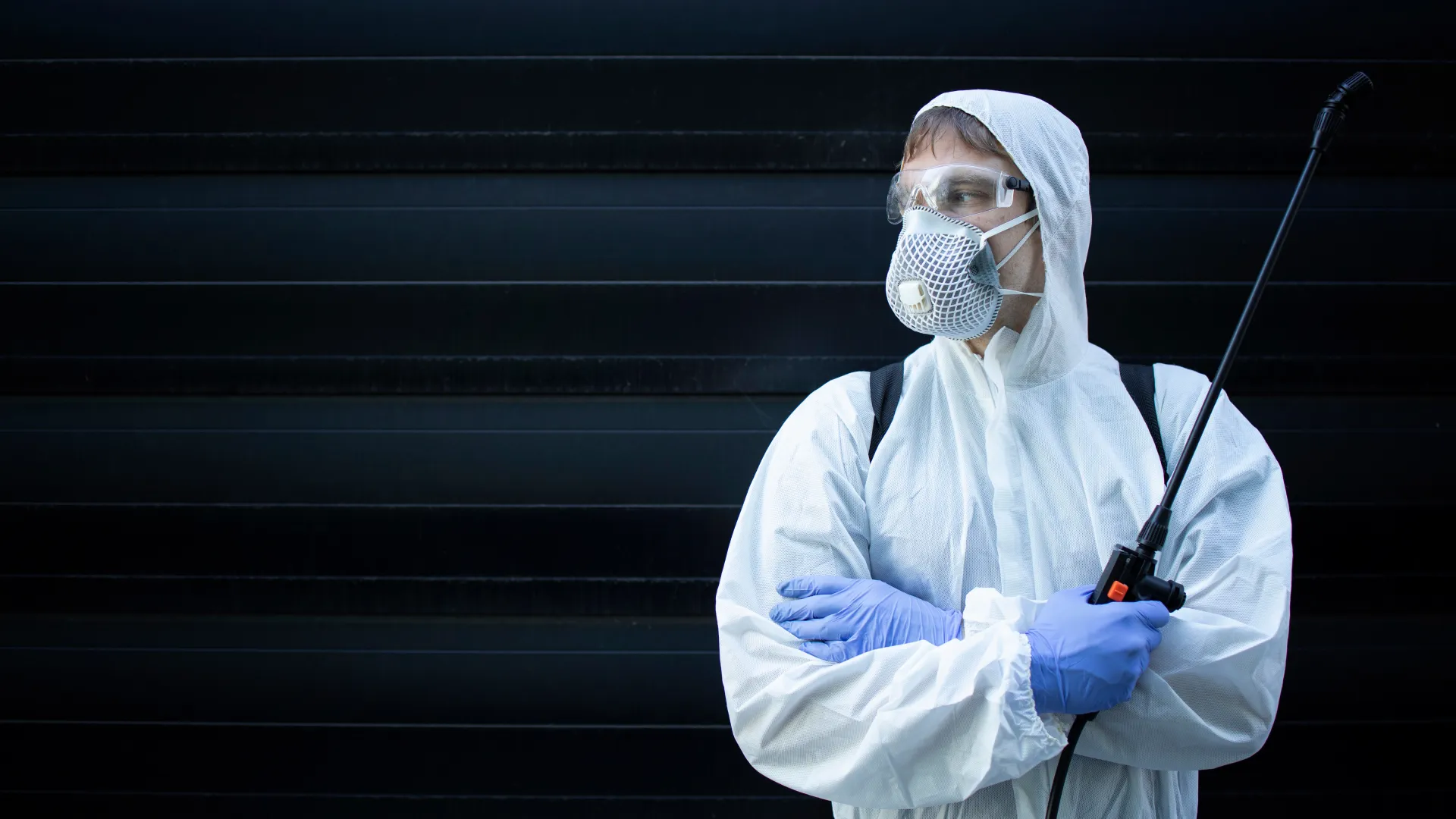 A person in protective gear stands confidently, holding a spray device against a dark background.