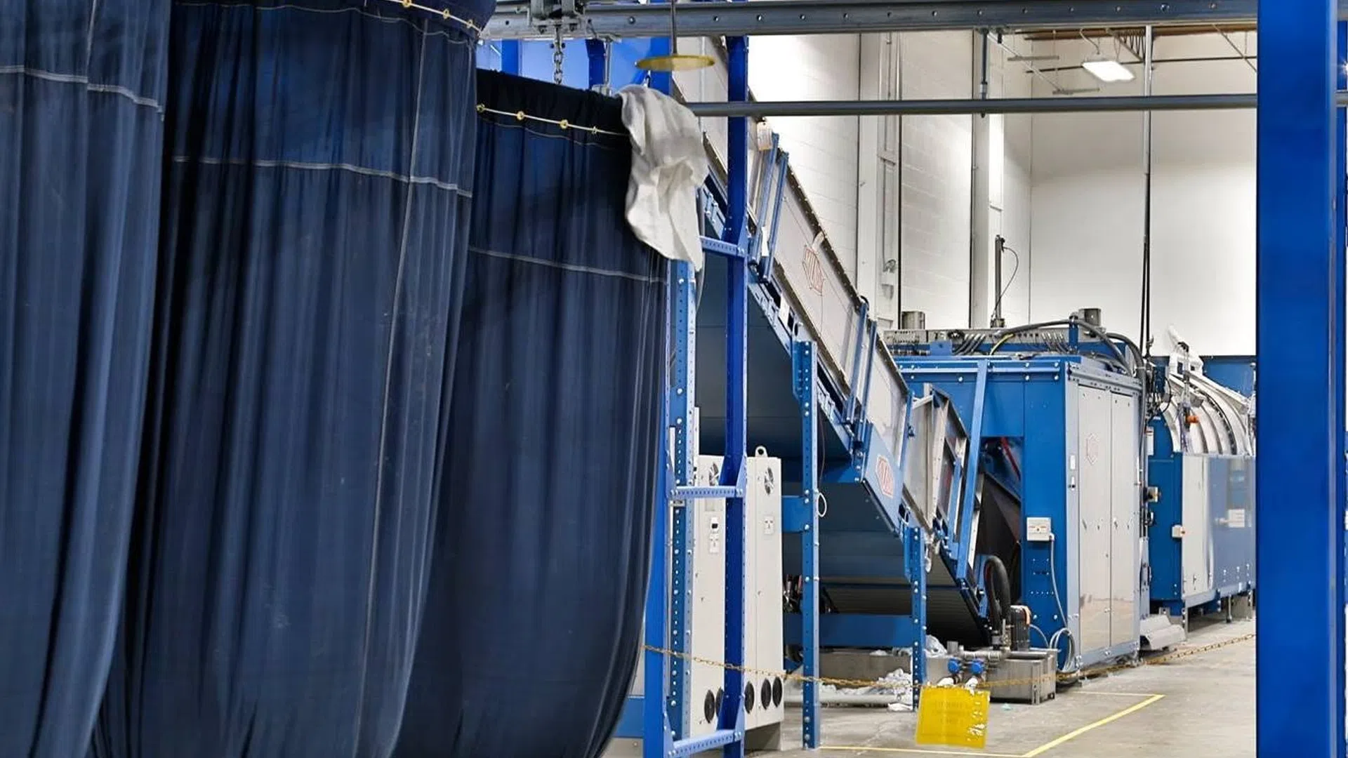 Industrial laundry facility with large blue textile bags and conveyor machinery in a factory setting
