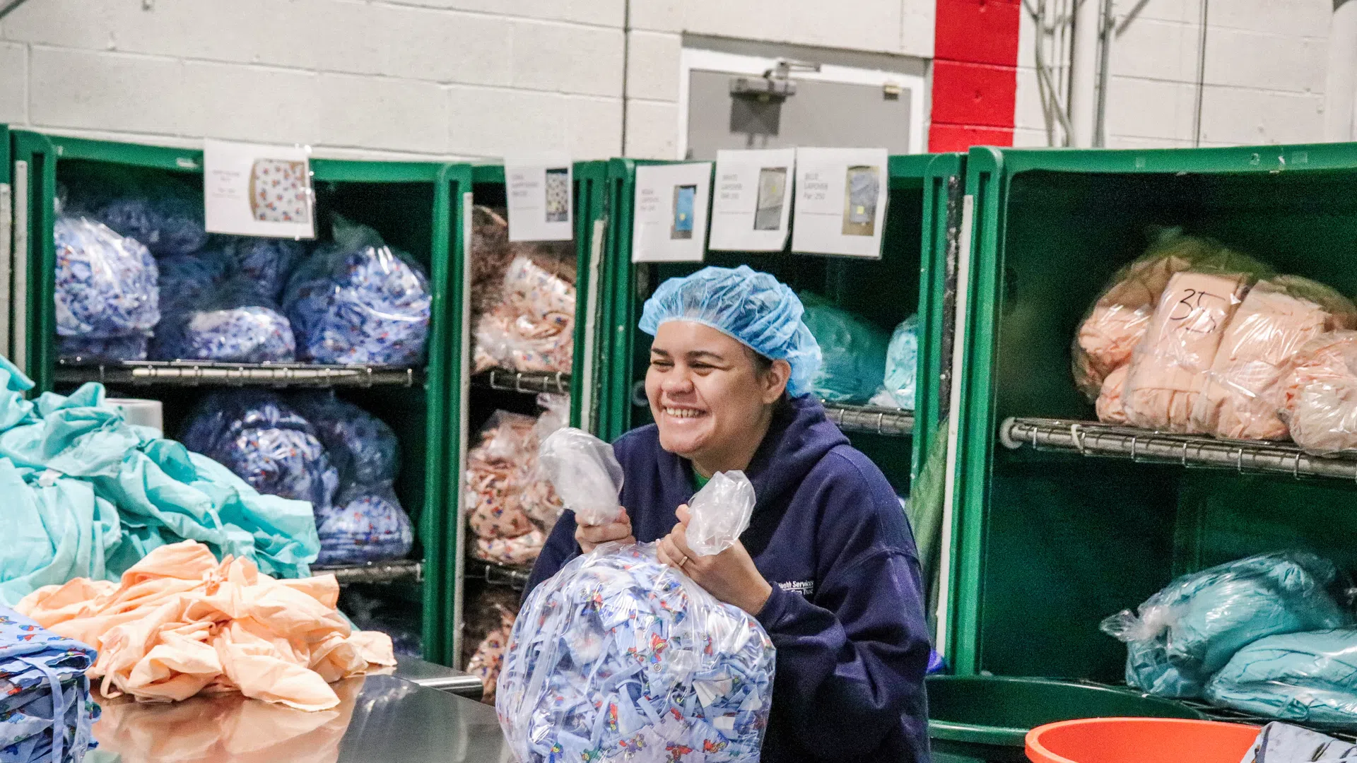 Worker in hairnet packing fabric bundles in a textile factory with shelves of sorted materials behind.