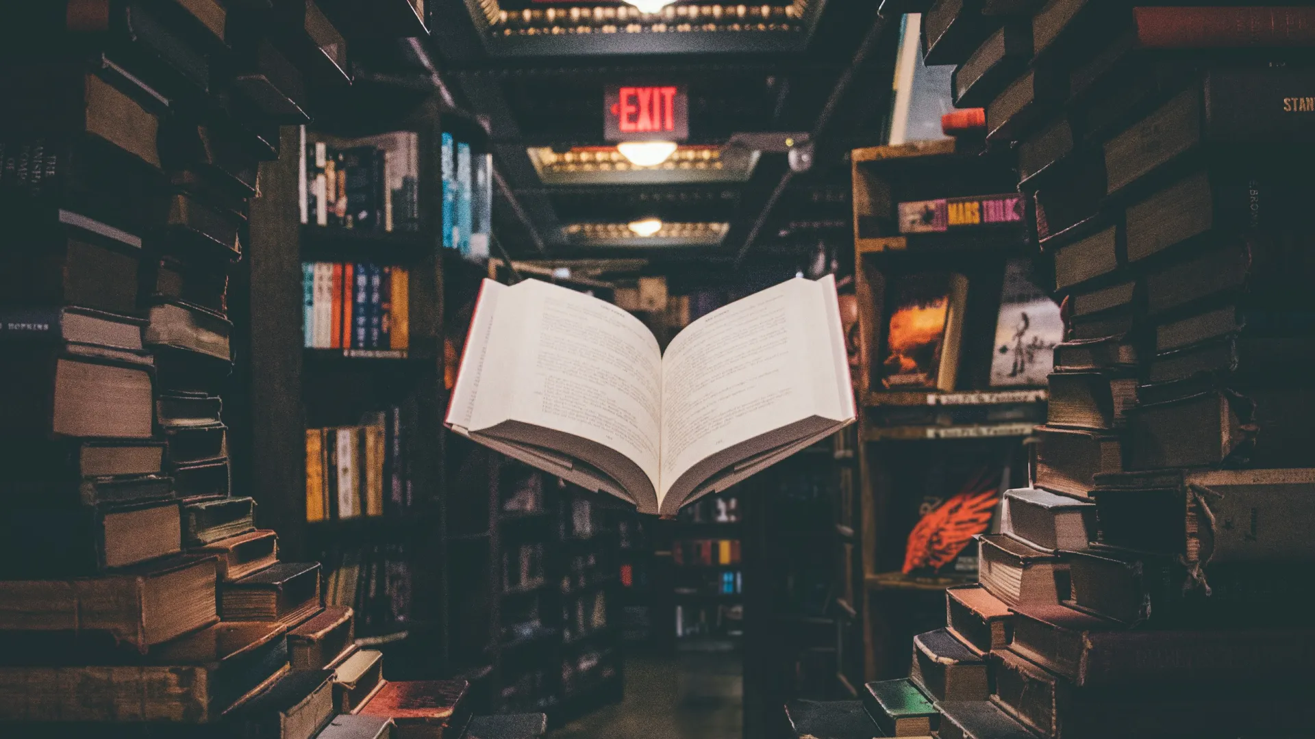 Open book suspended in midair surrounded by stacks of books forming an archway inside a dimly lit library.