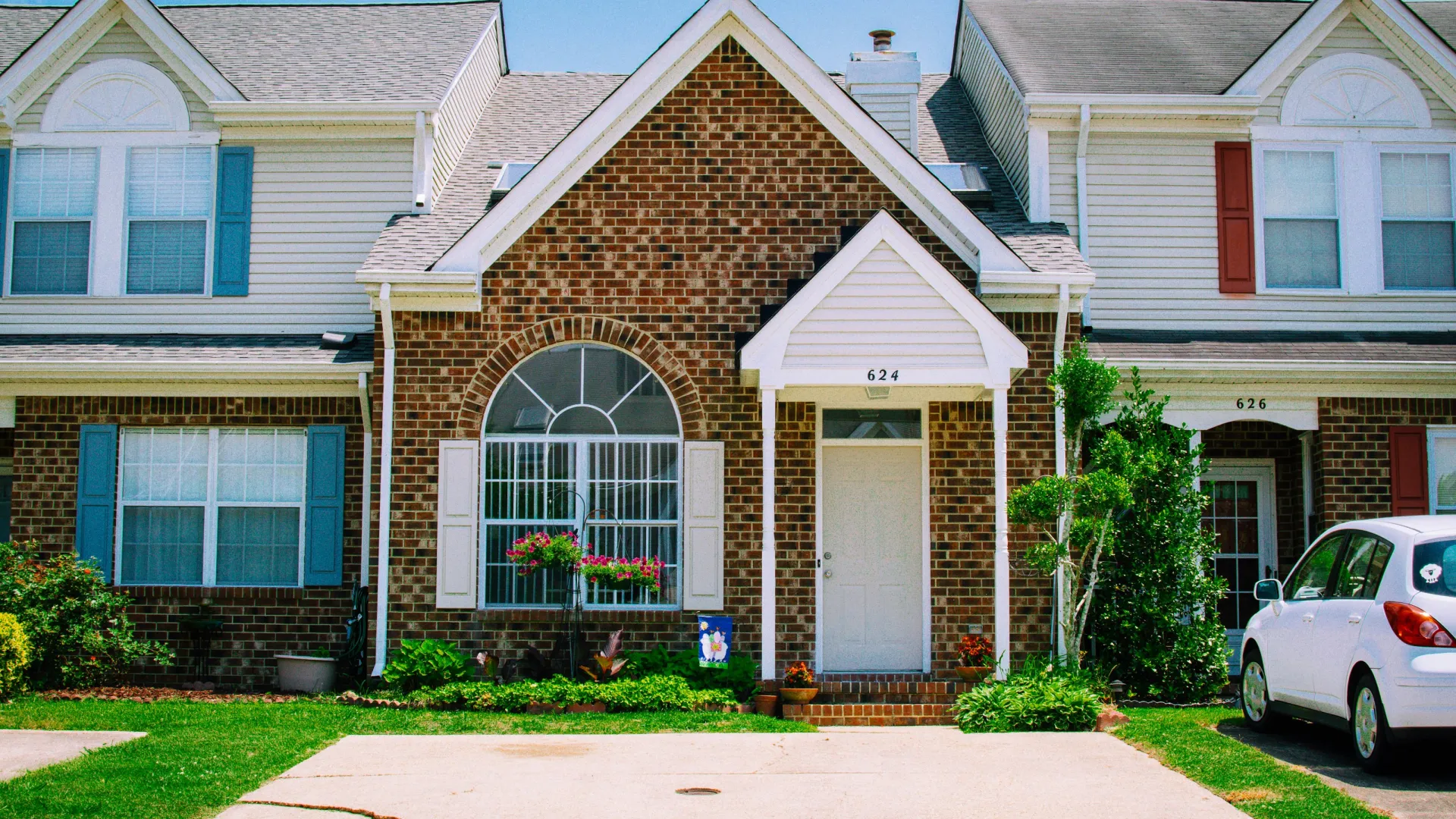 Brick townhouse with white door, arched window, and green plants on a sunny day with blue sky