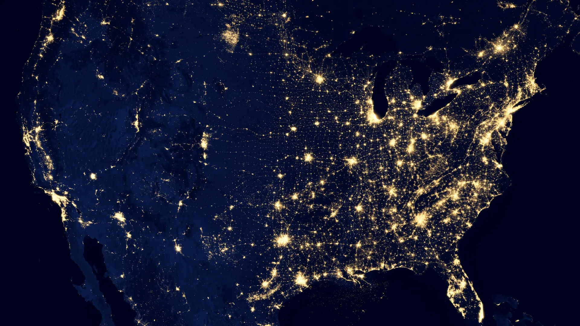 Satellite view of the United States at night showing city lights and urban areas brightly illuminated.
