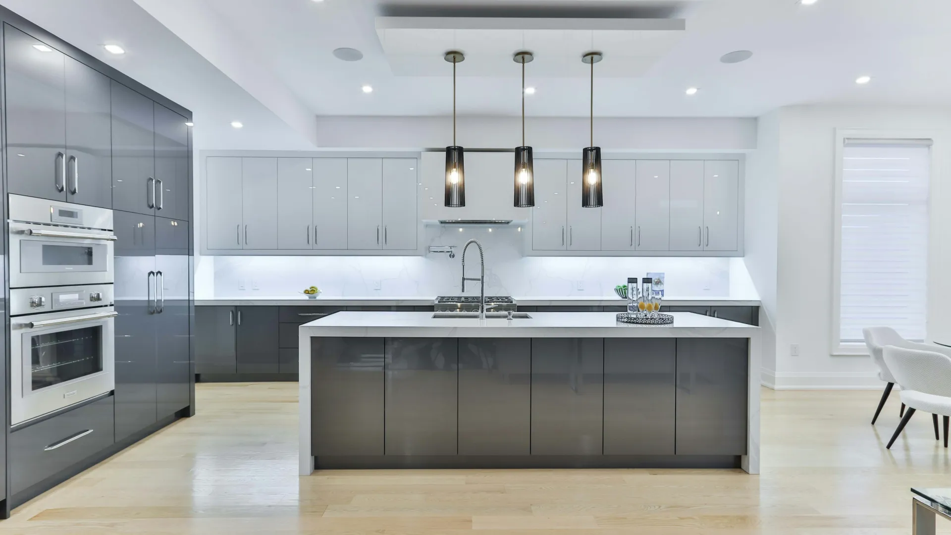 Modern kitchen with gray and white cabinets, central island, pendant lights, built-in oven, and light wood flooring