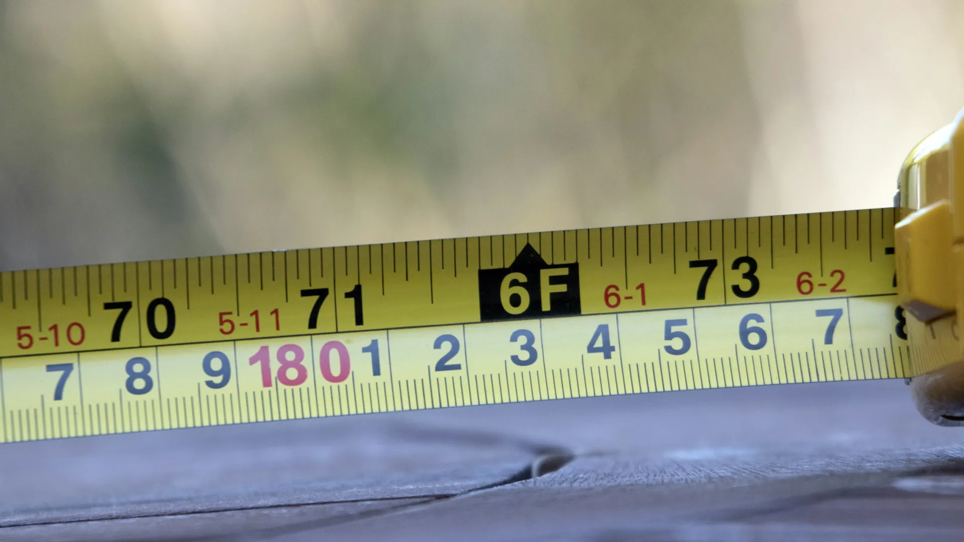 Close-up of yellow tape measure showing 6 feet and 180 centimeters on a blurred background.